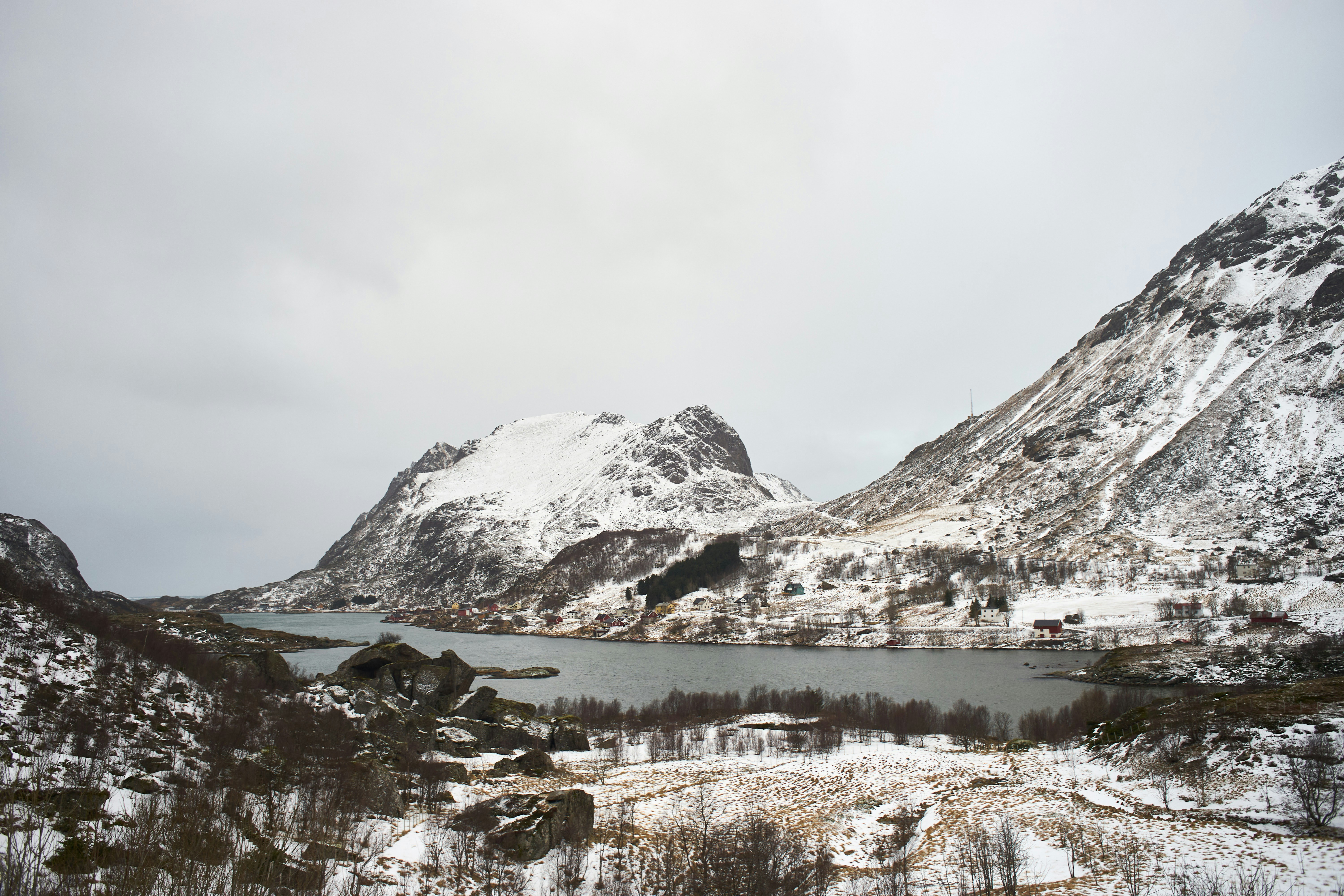 Snow-covered mountains surround a calm lake under a grey sky.