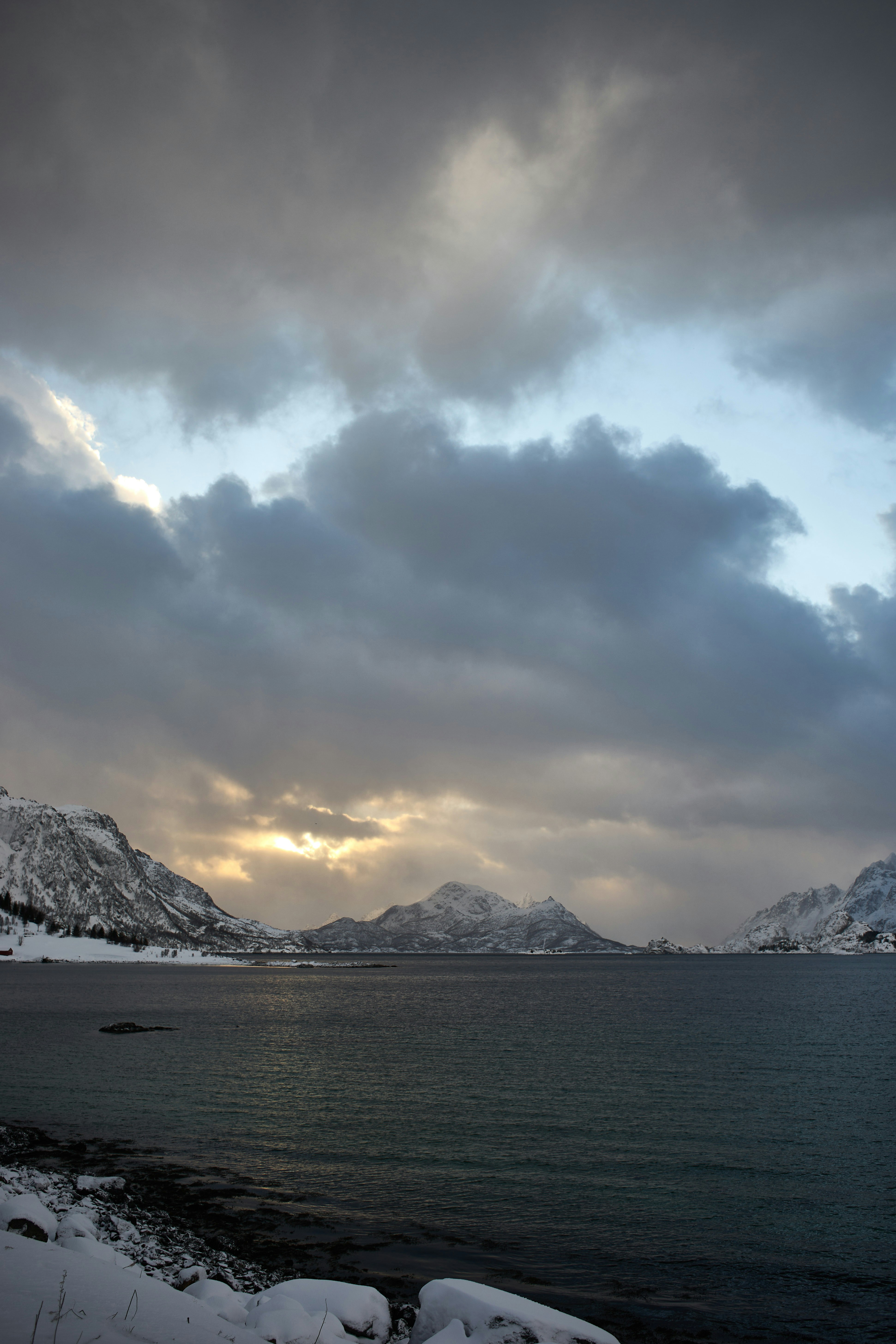 Snowy mountains overlook a dark, choppy ocean under cloudy skies.
