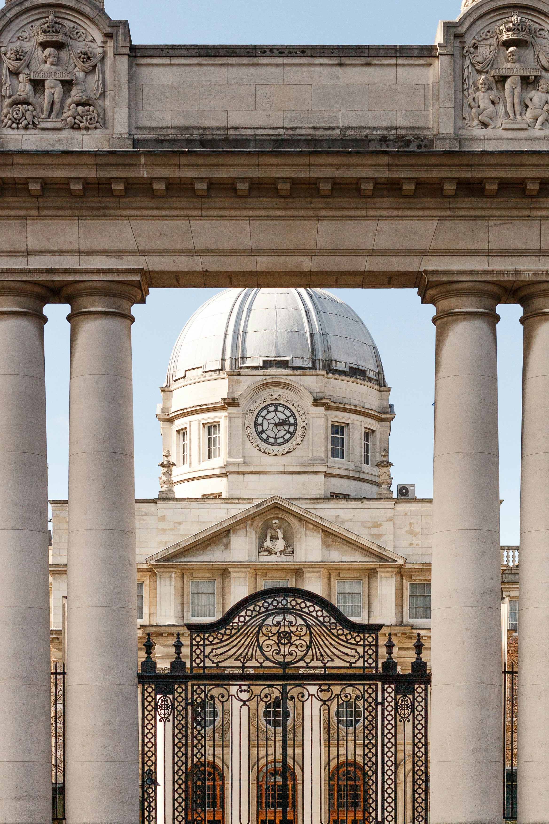 Grand building with dome and clock behind ornate gate.
