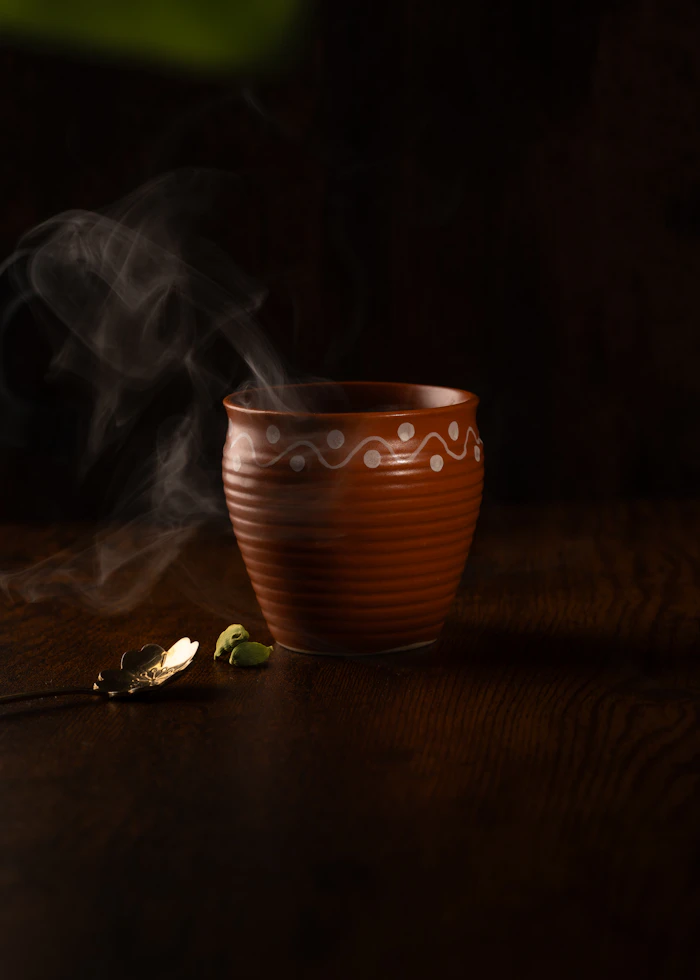 Thé chai fumant dans une tasse en terre cuite avec de la cardamome