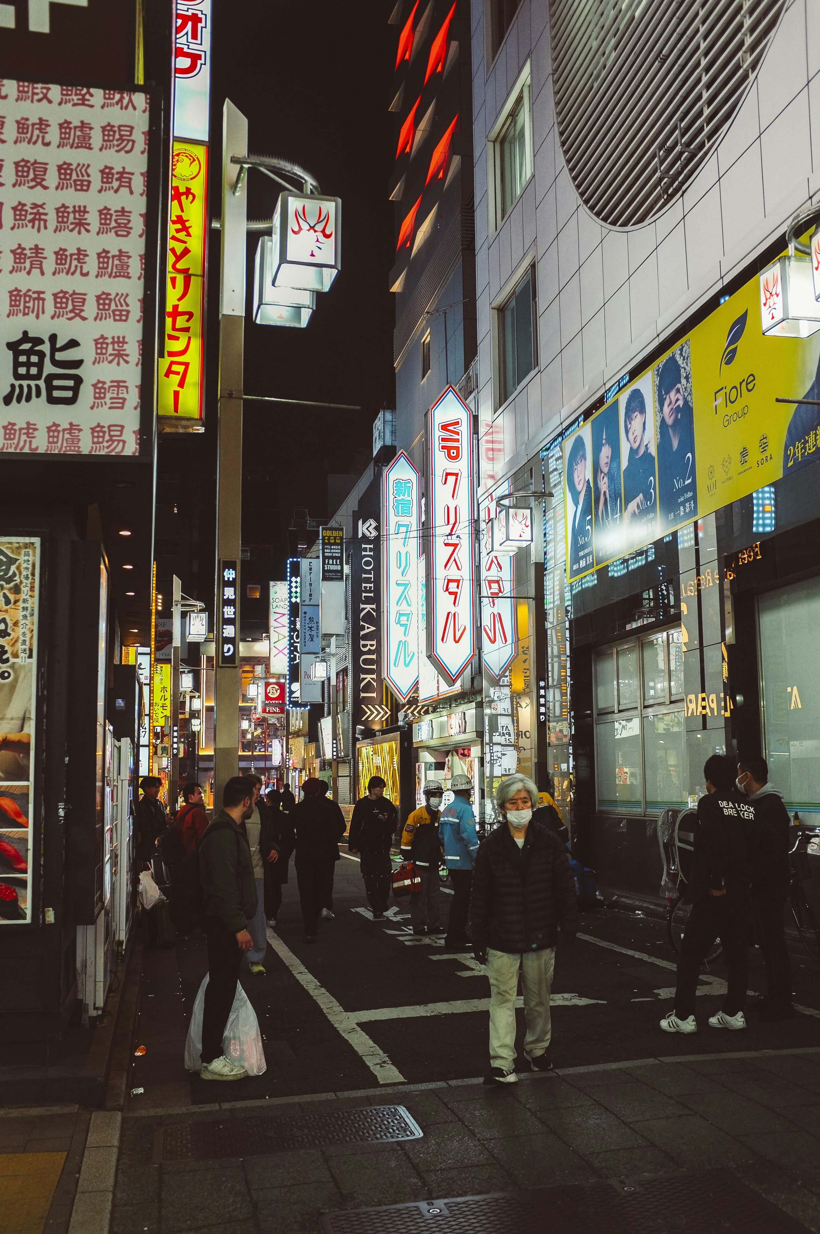 People walk down a neon-lit street at night.