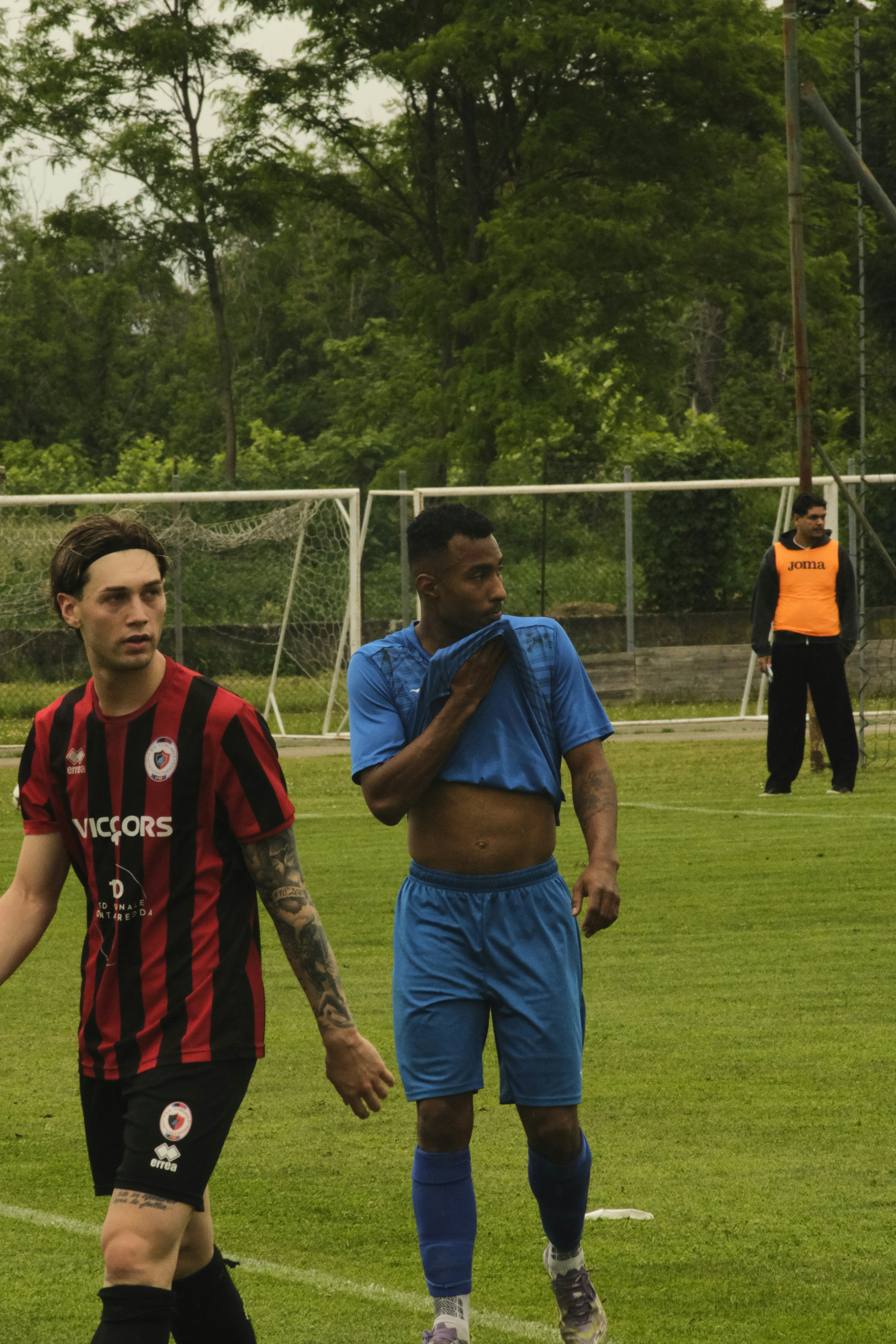 Dua pemain sepak bola di lapangan, satu menyeka wajahnya.