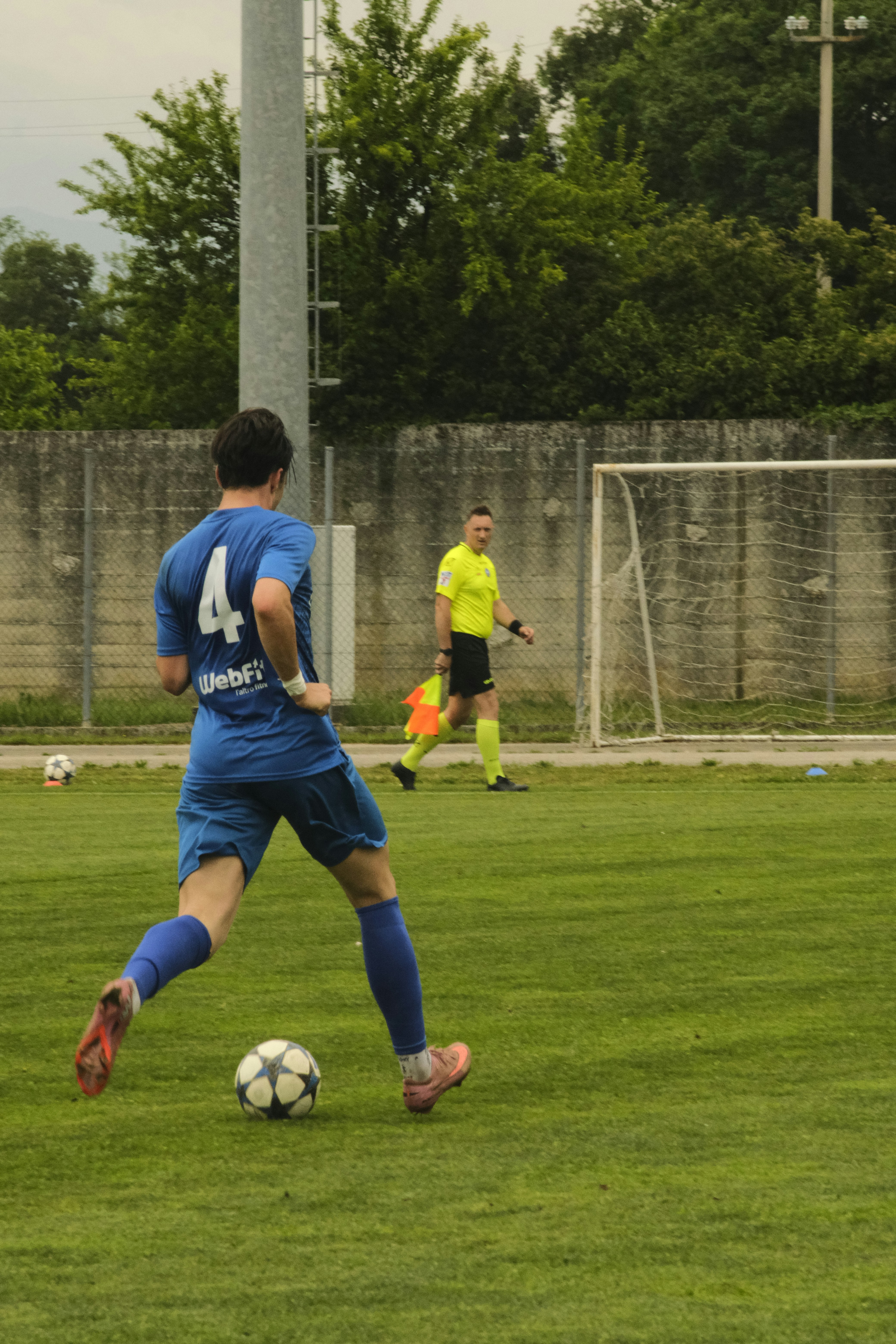 A soccer player in blue uniform kicks ball on field