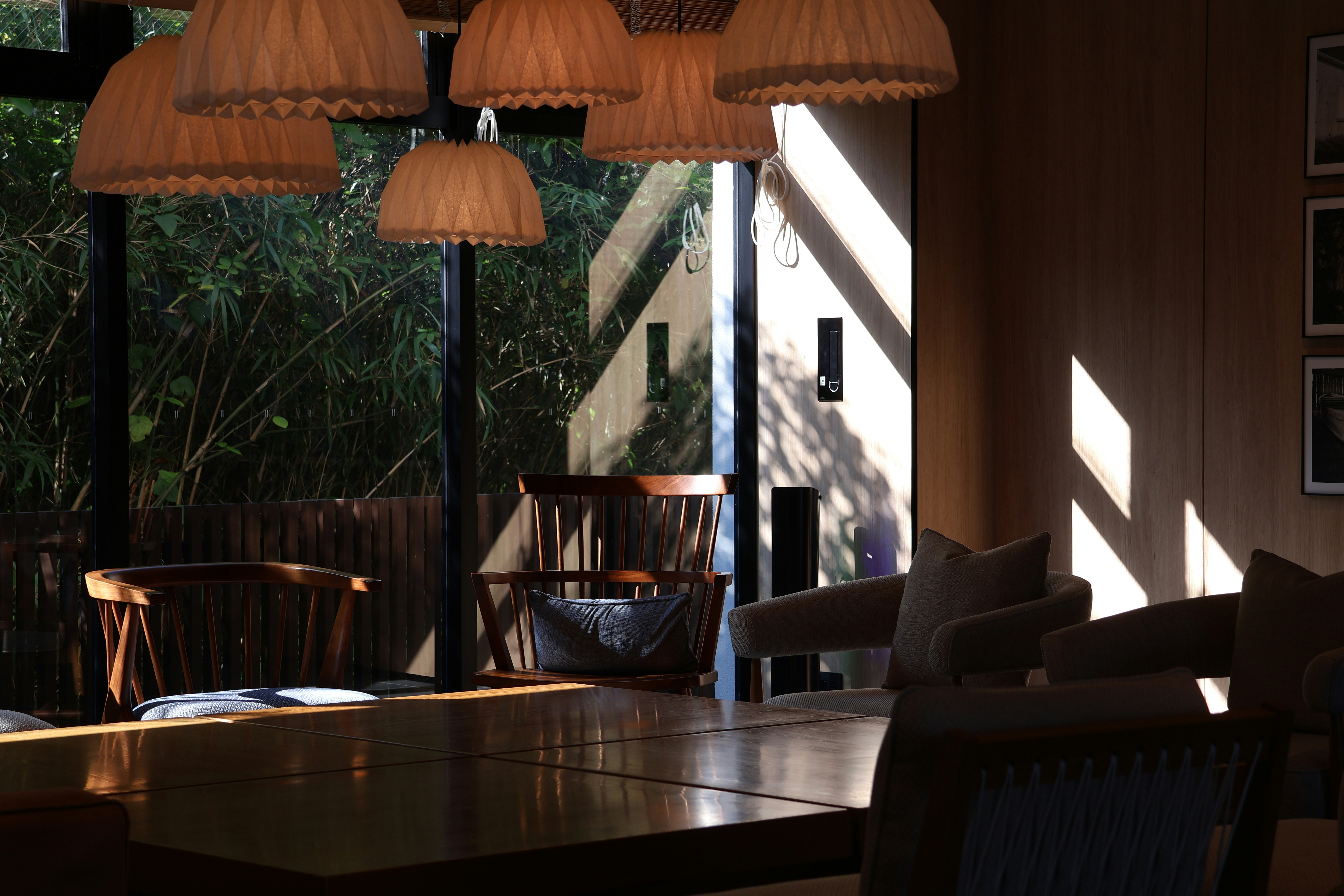Quarto iluminado pelo sol, com luminárias trançadas, móveis de madeira e vista para o exterior.