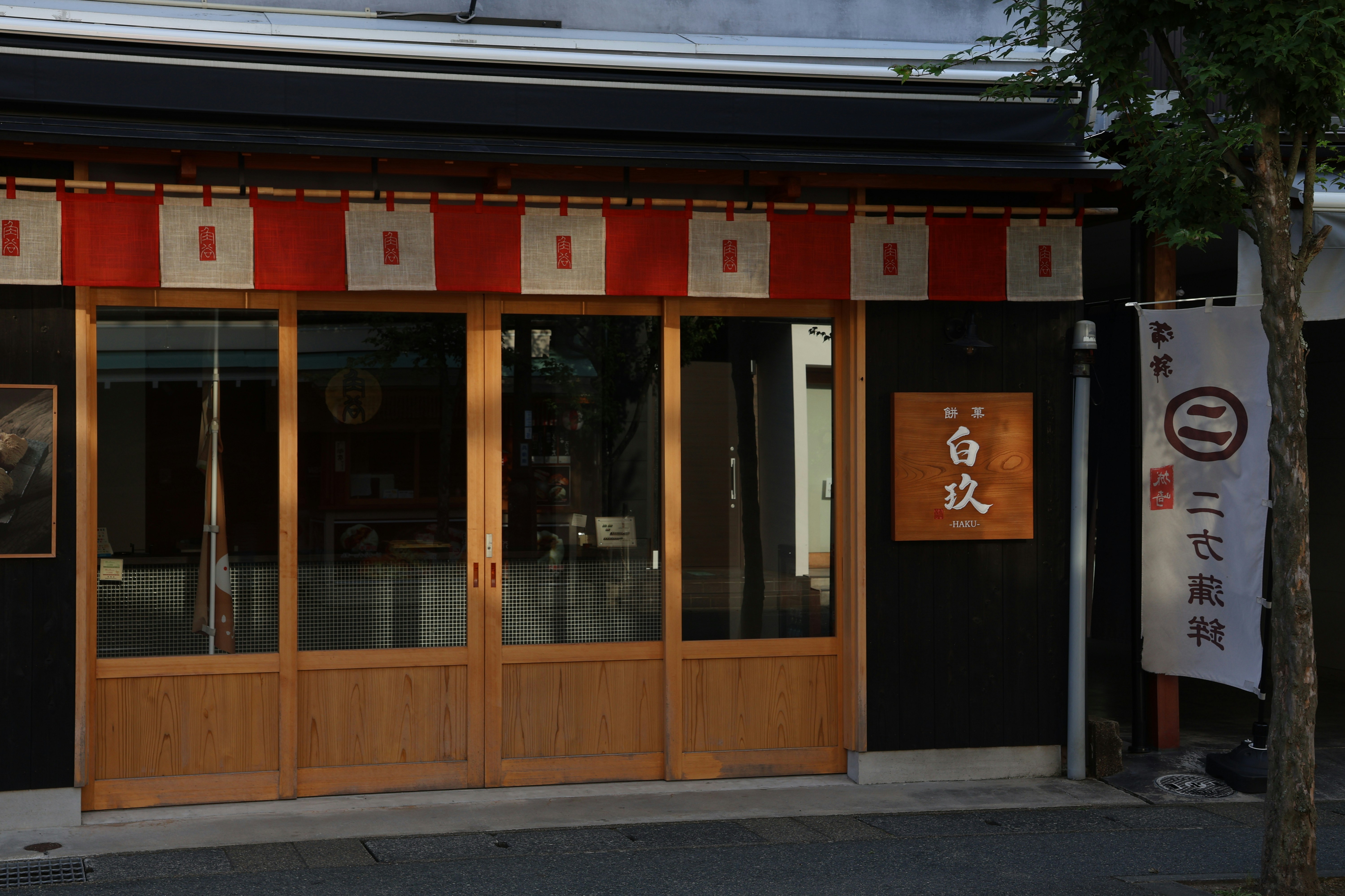 Fachada de loja com portas de madeira, toldo vermelho e sinalização japonesa.
