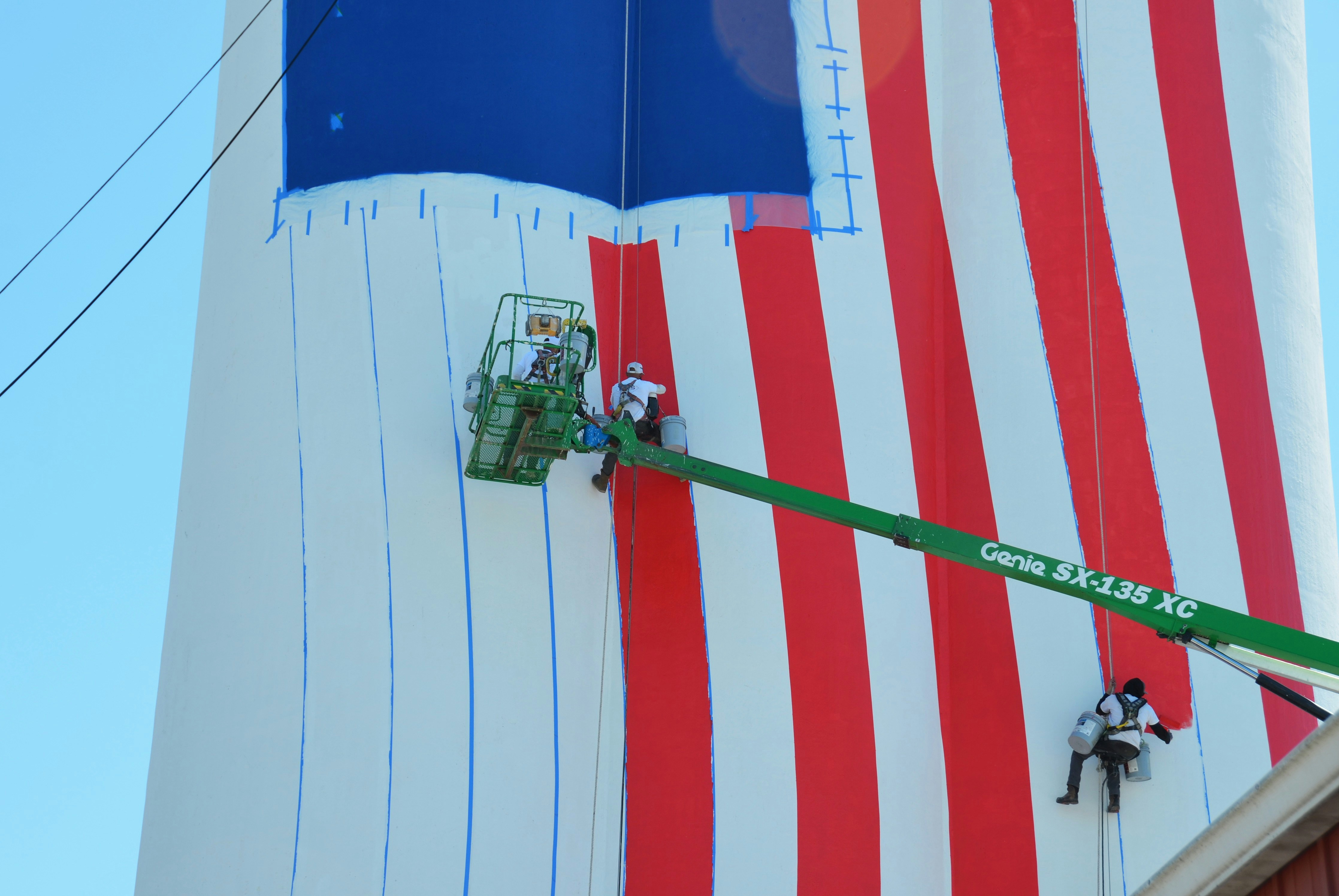 Los trabajadores pintan una enorme bandera estadounidense en una estructura alta.