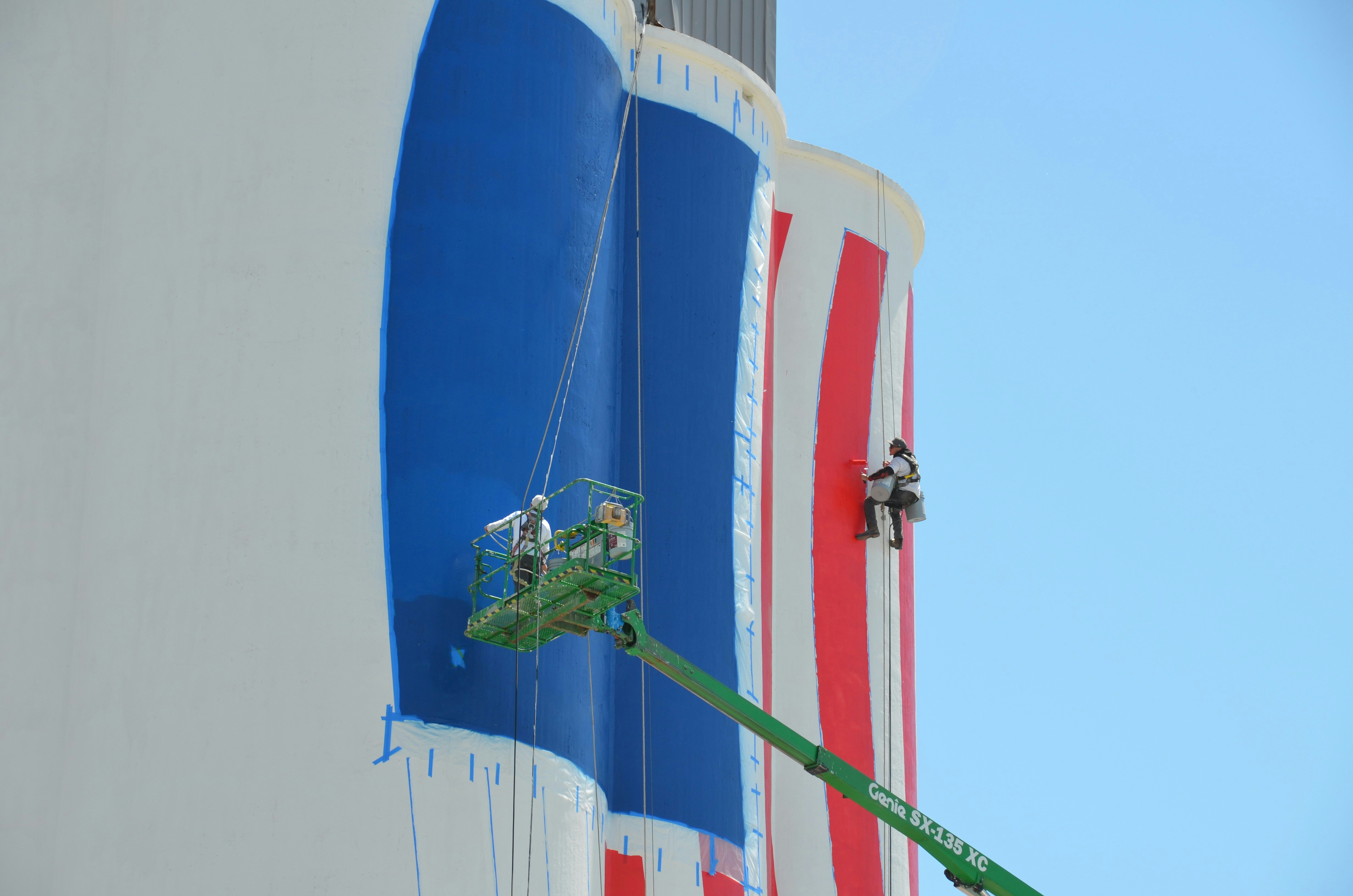 Workers painting a large blue and red striped structure