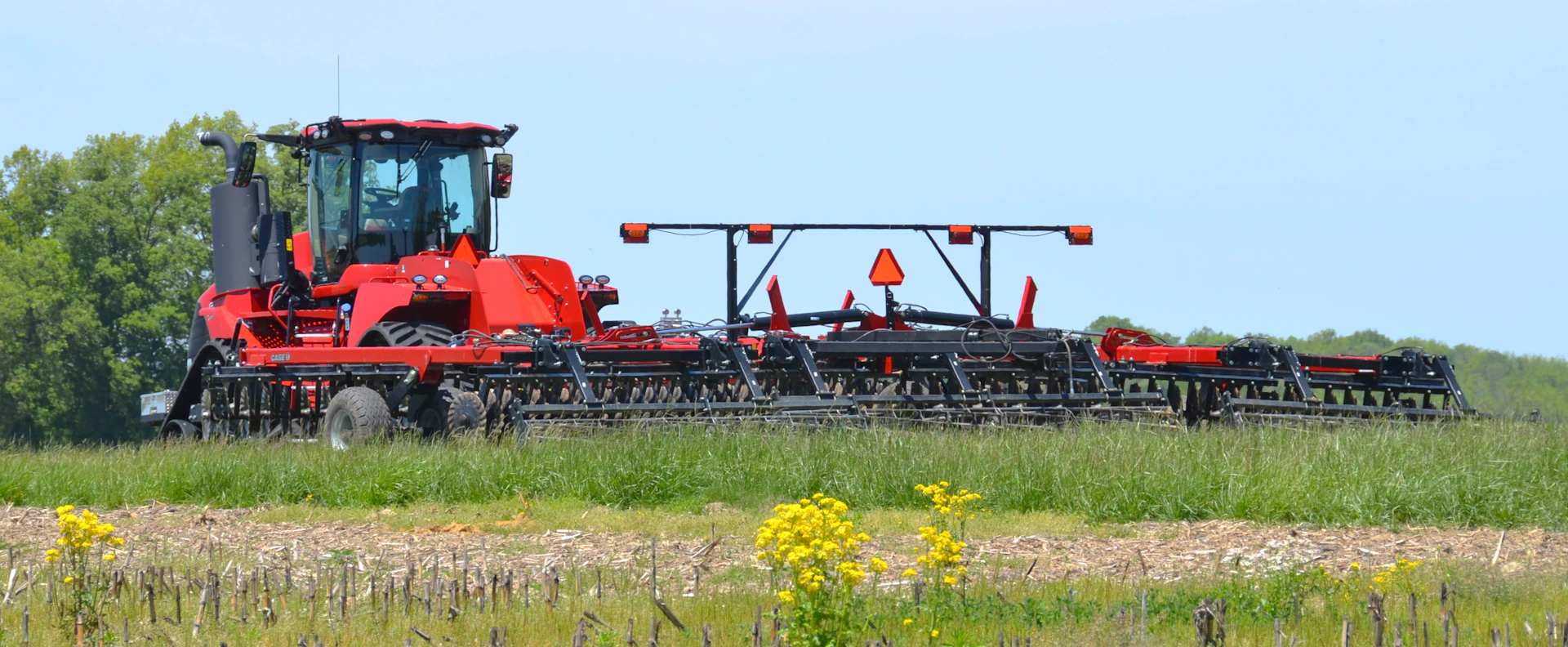 A red tractor with farm equipment in a green field.