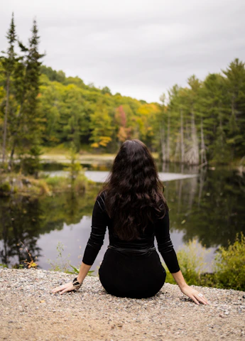 Woman in black dress sitting by a lake