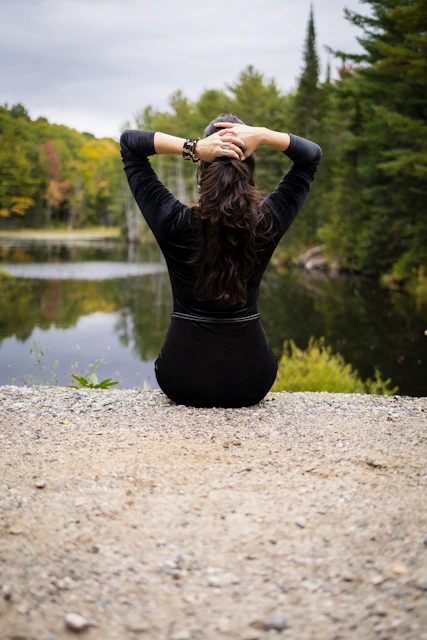 Woman sitting by a lake with hands behind head