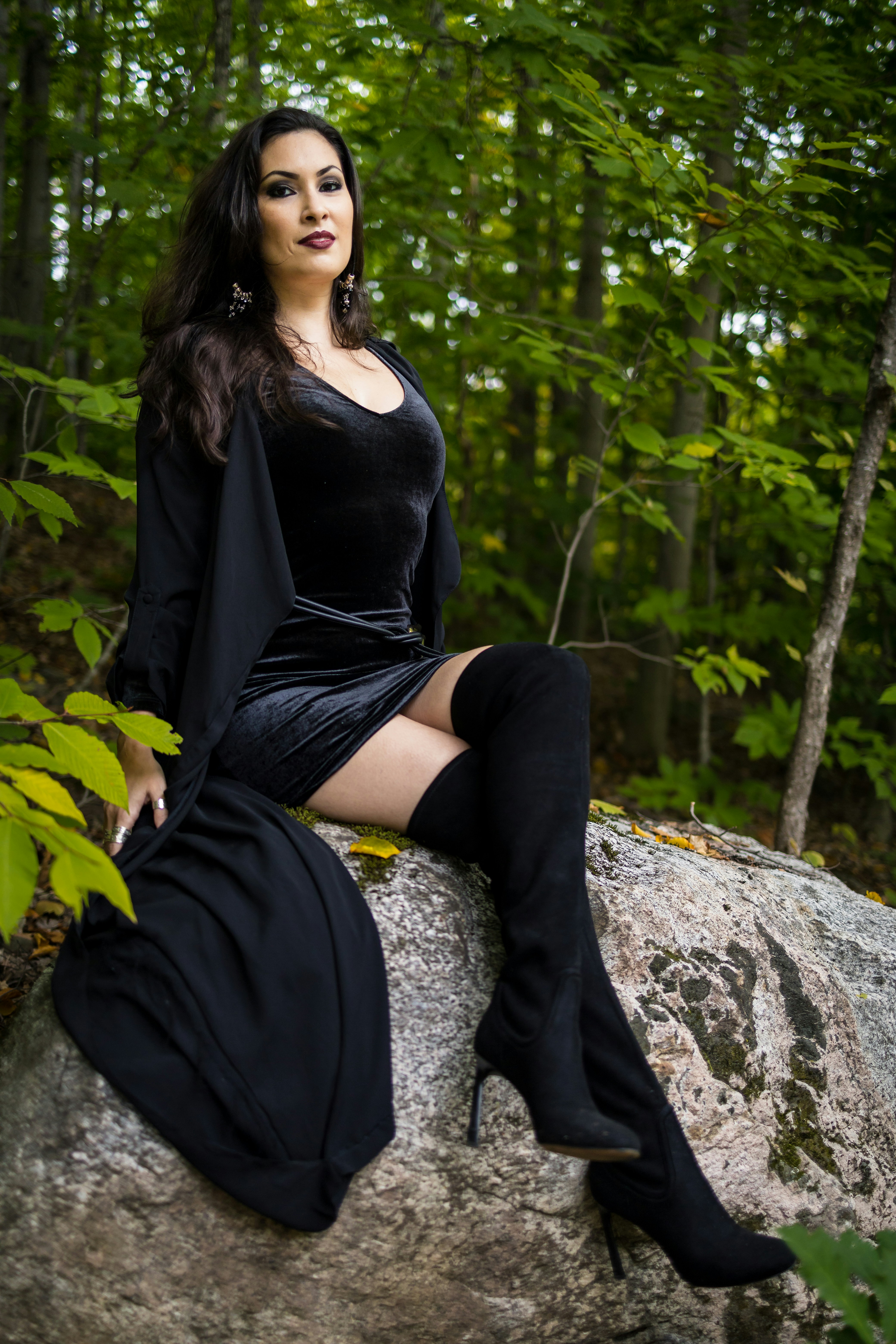 Frau in schwarzem Kleid und Stiefeln sitzt auf Felsen