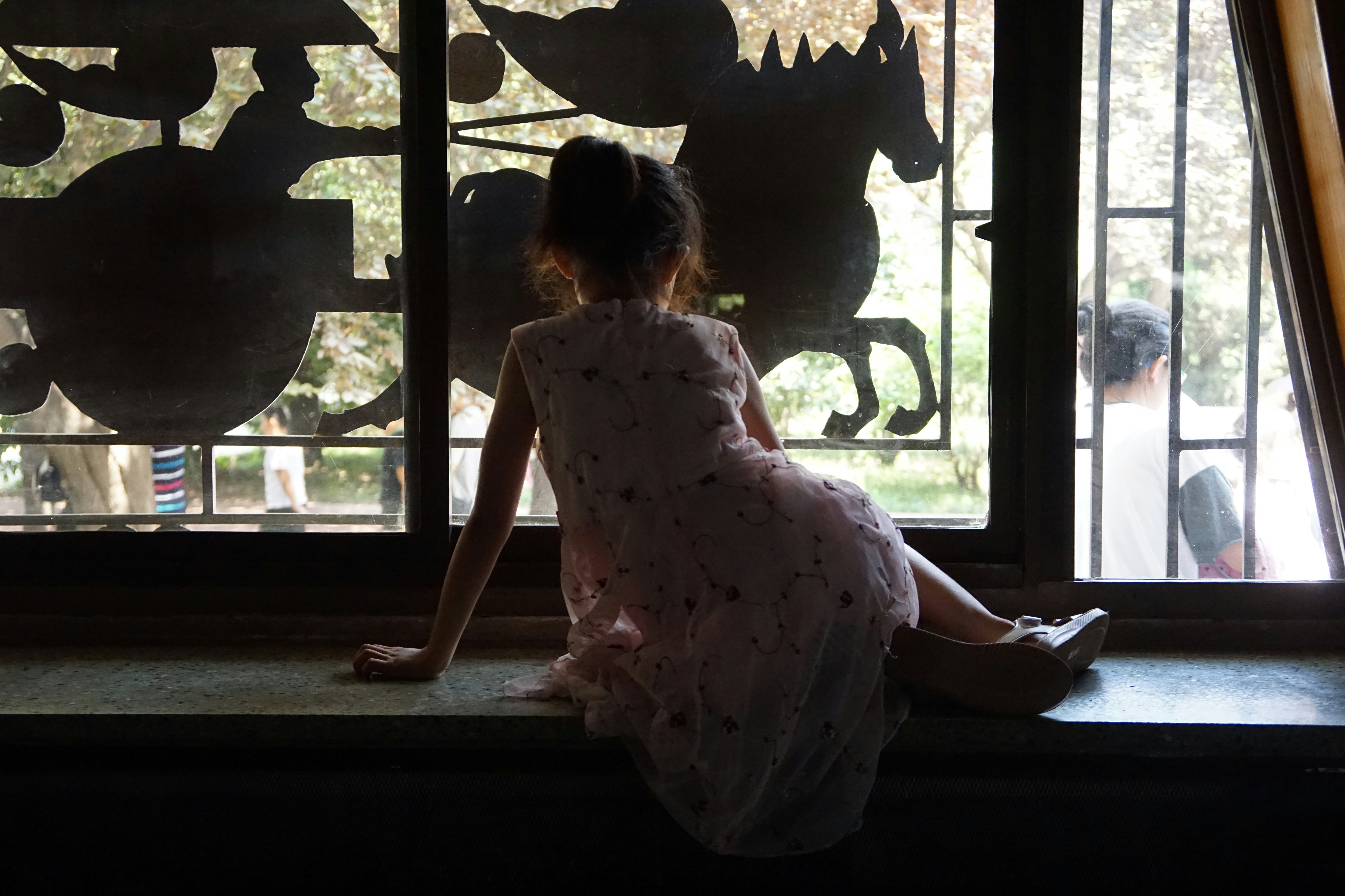 Girl in dress looks out ornate window at park