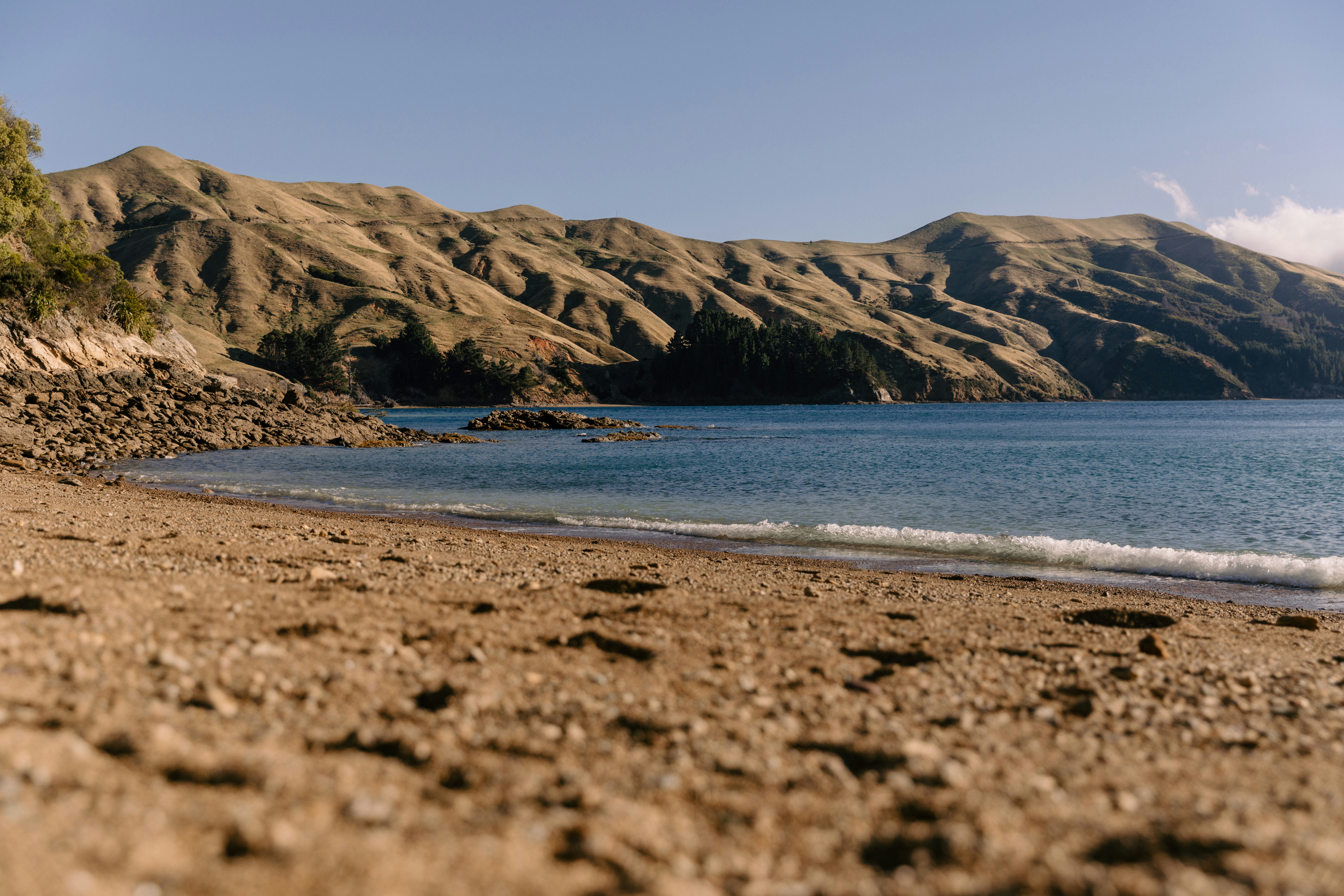 Dry hills overlook a sandy beach and calm blue bay.