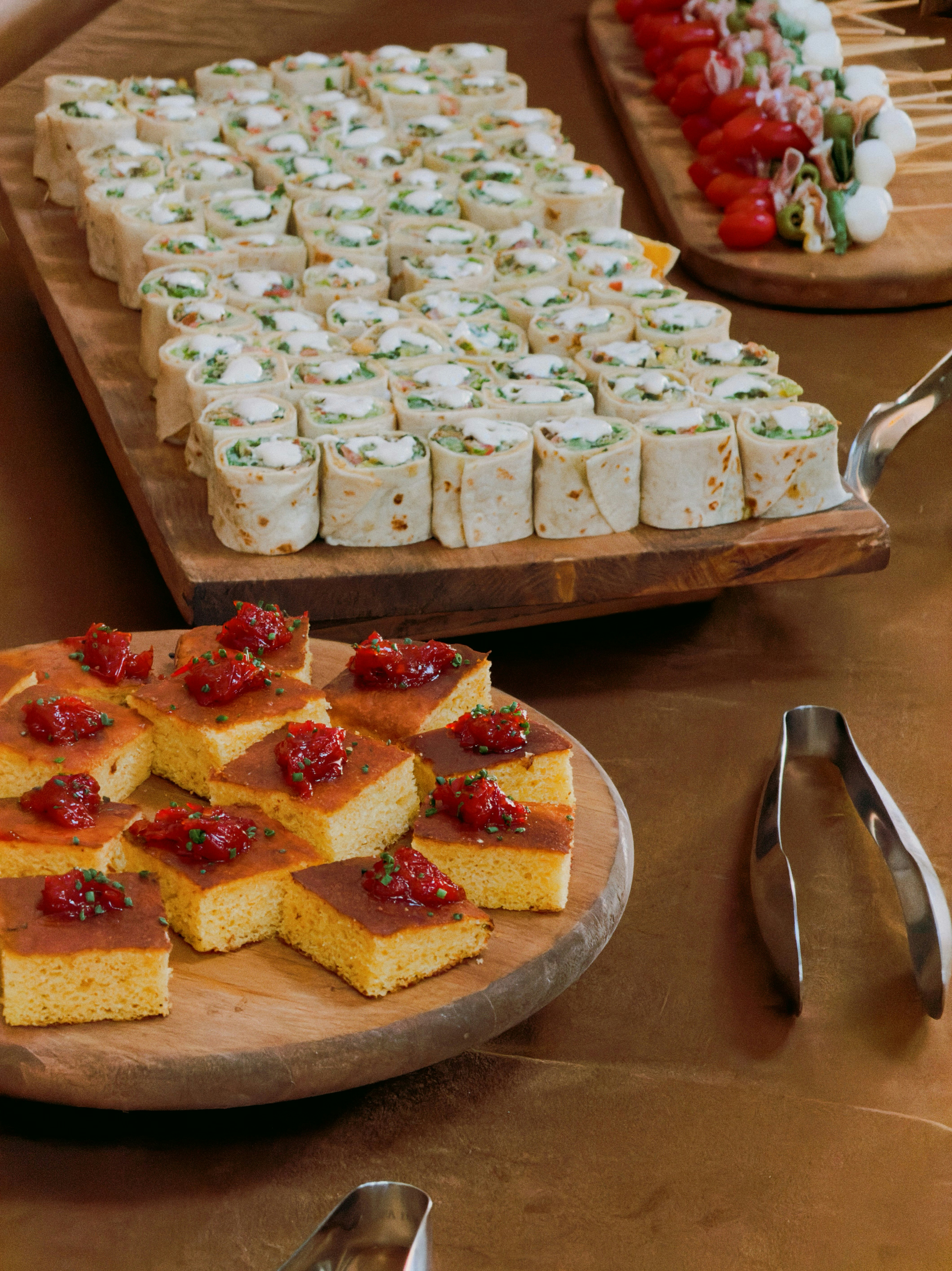 Catering spread with savory rolled wraps and sweet square cakes.