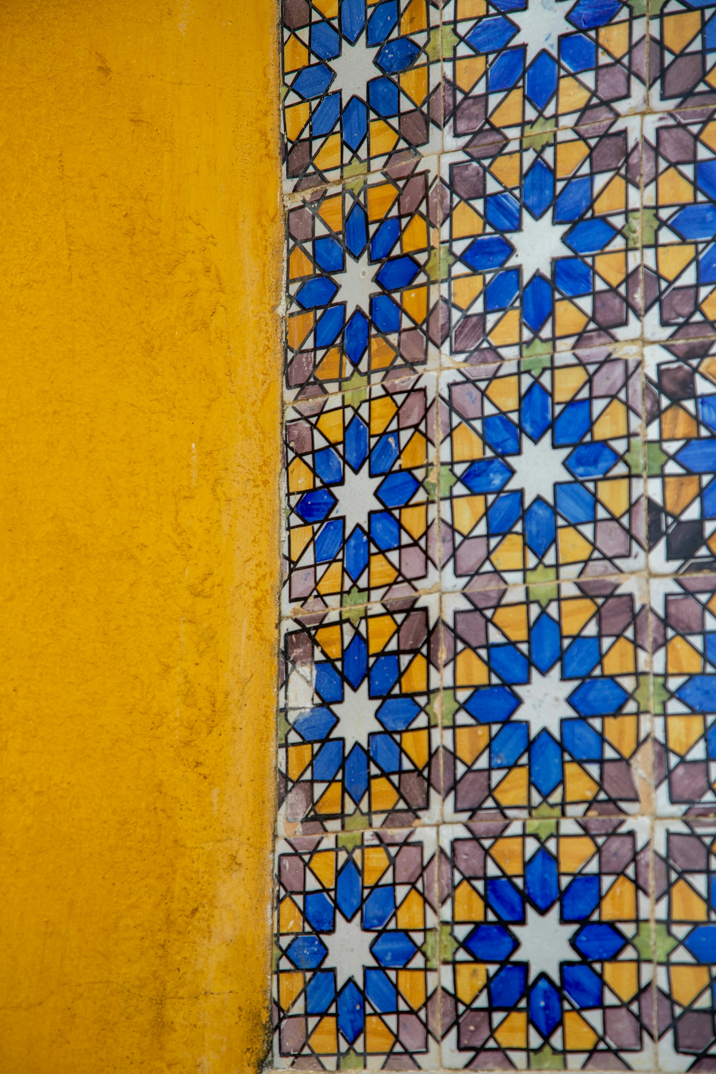 Dinding kuning di samping ubin berpola geometris berwarna-warni