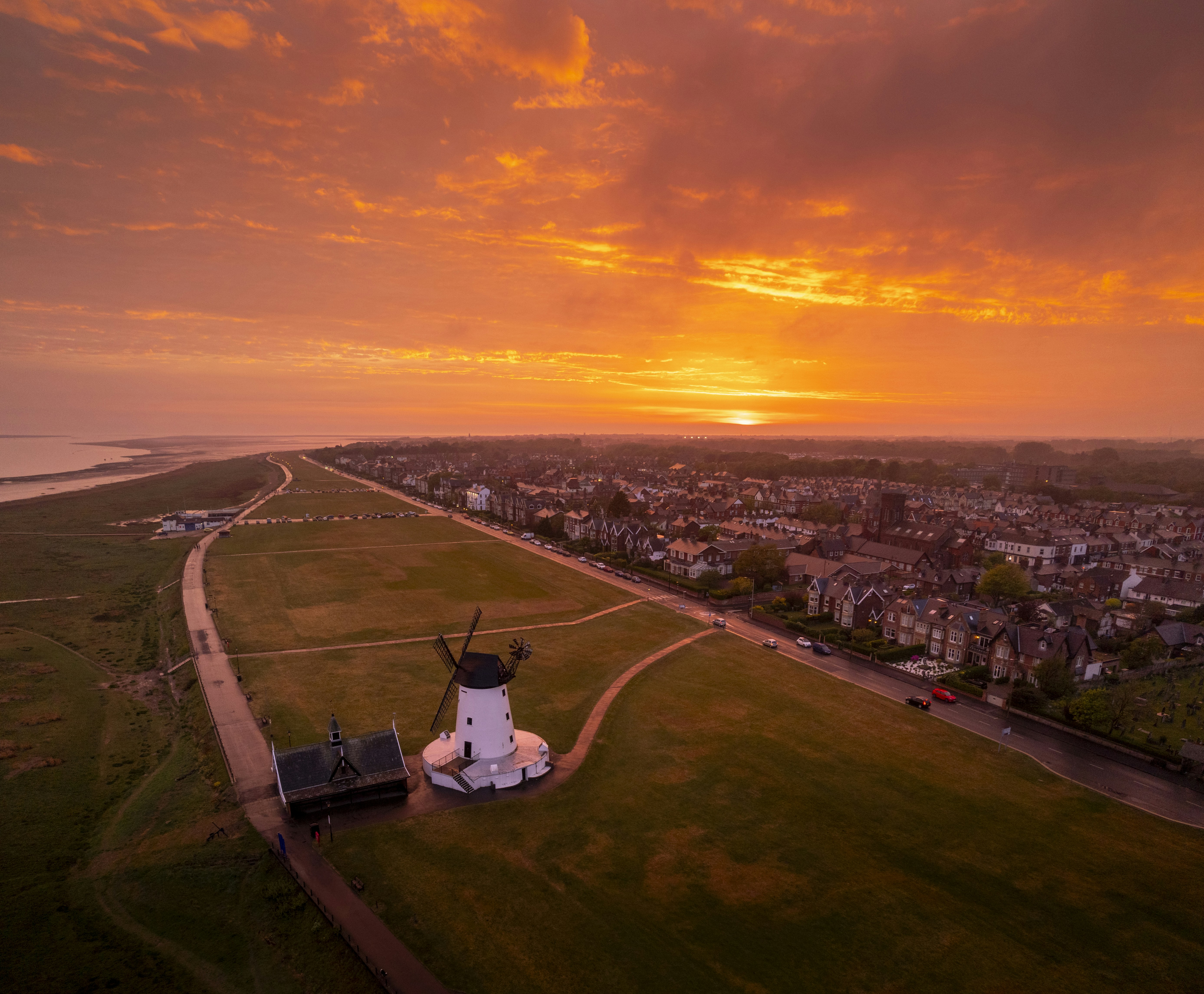 Vibrant sunset over a coastal town with a windmill.