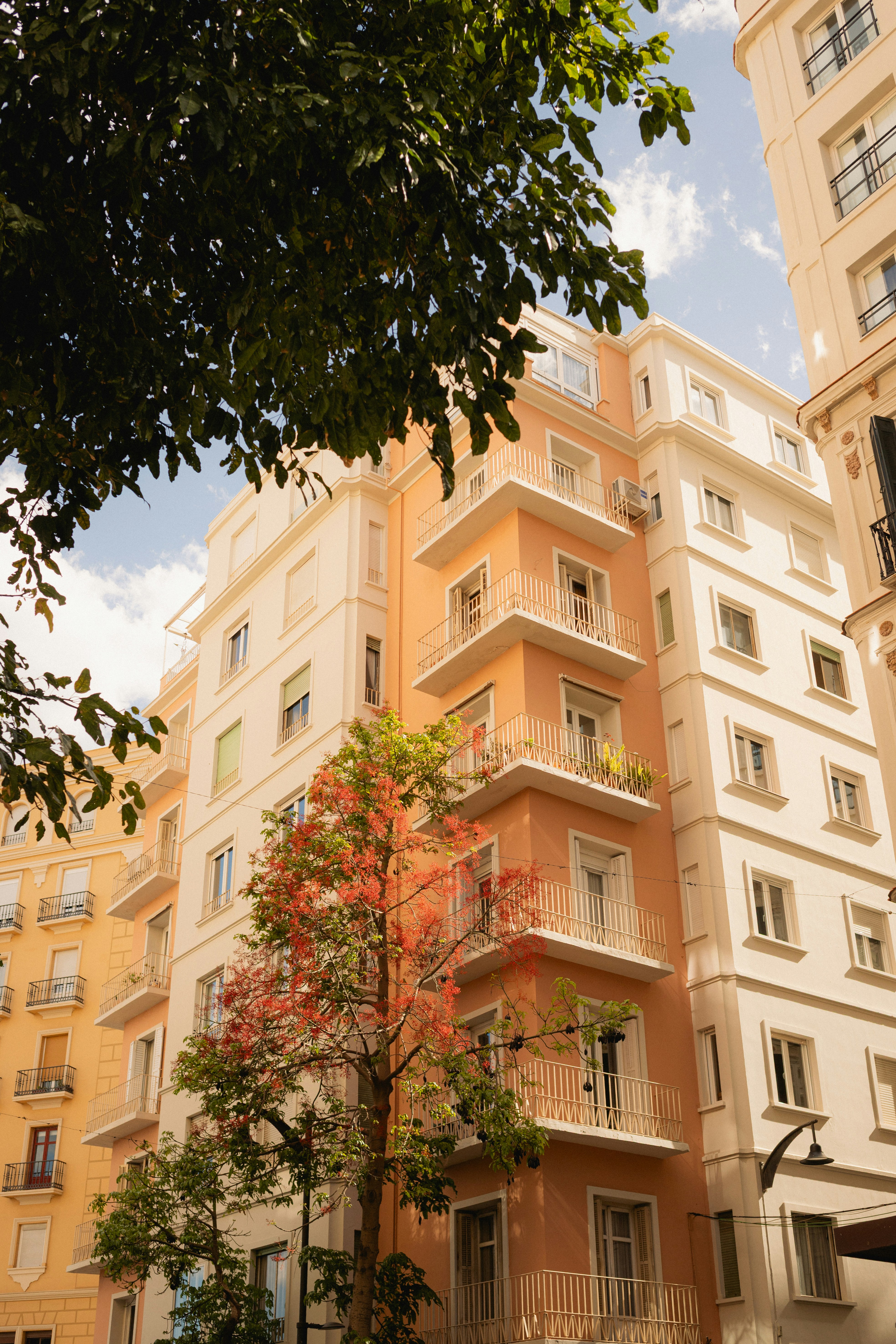 Gedung apartemen tinggi dengan balkon dan pepohonan.