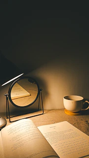 An open book, a cup of coffee, and a mirror.