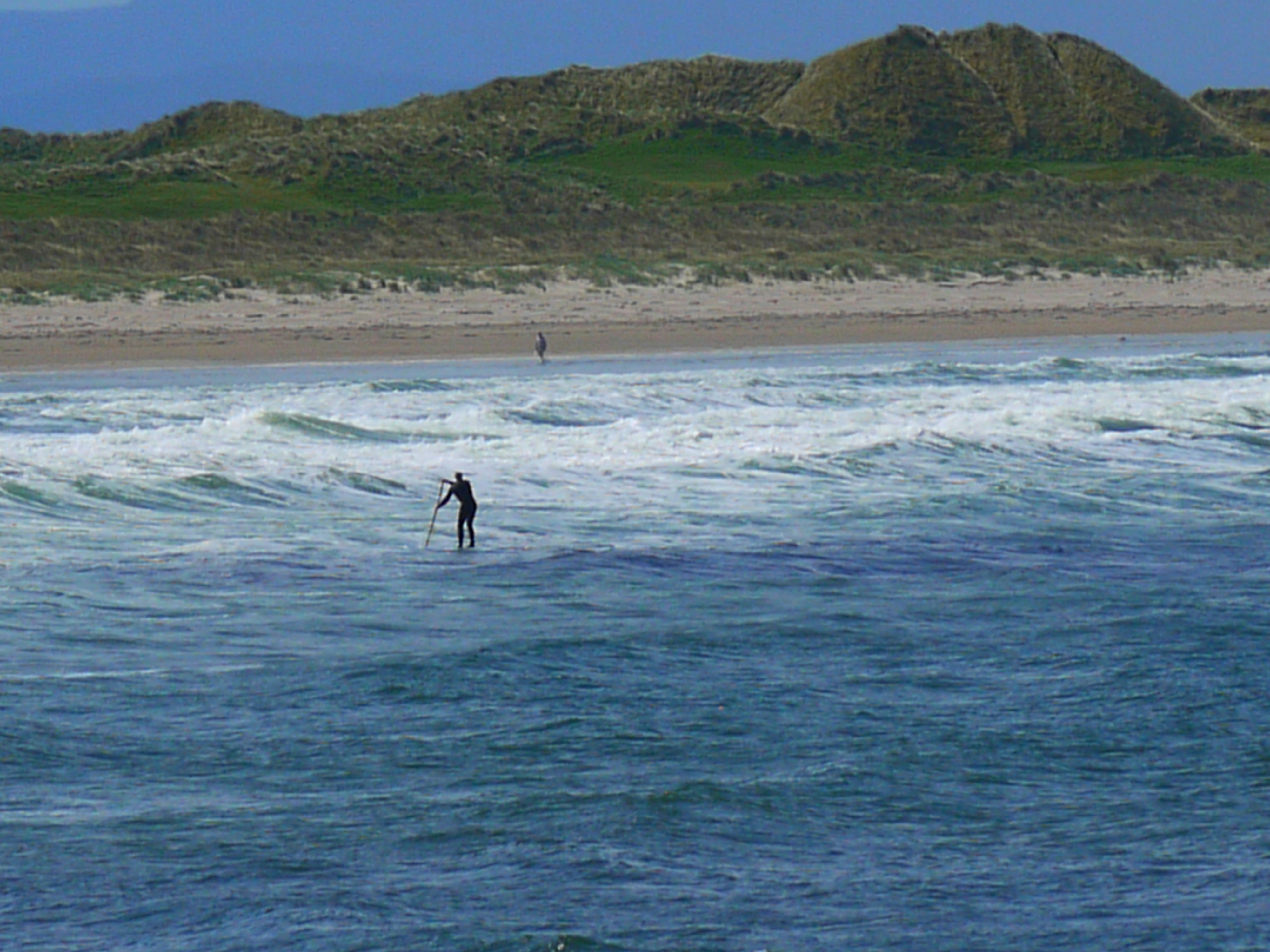 A person paddleboarding on the ocean near a sandy beach.