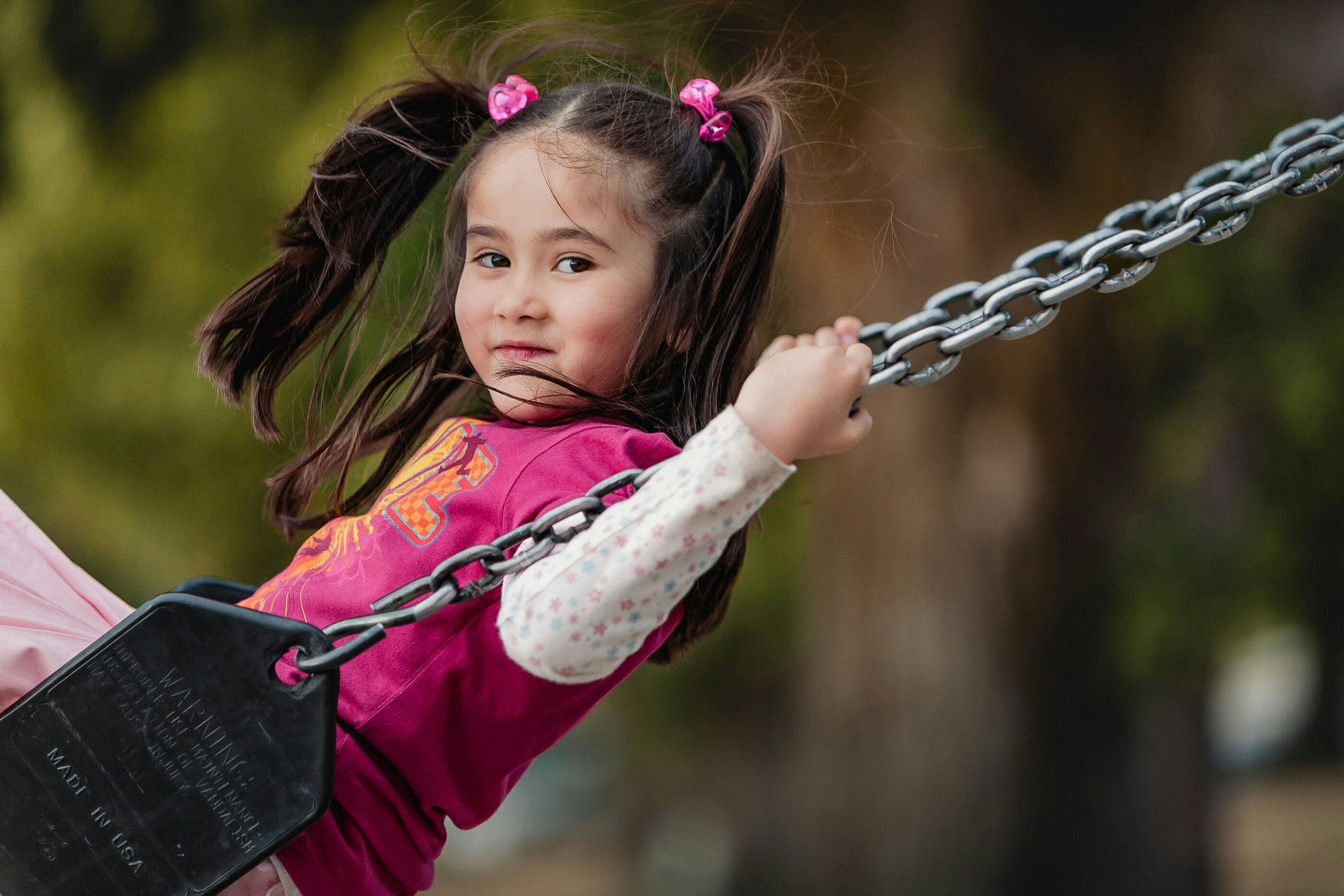 Little girl with pigtails enjoys swinging outdoors.