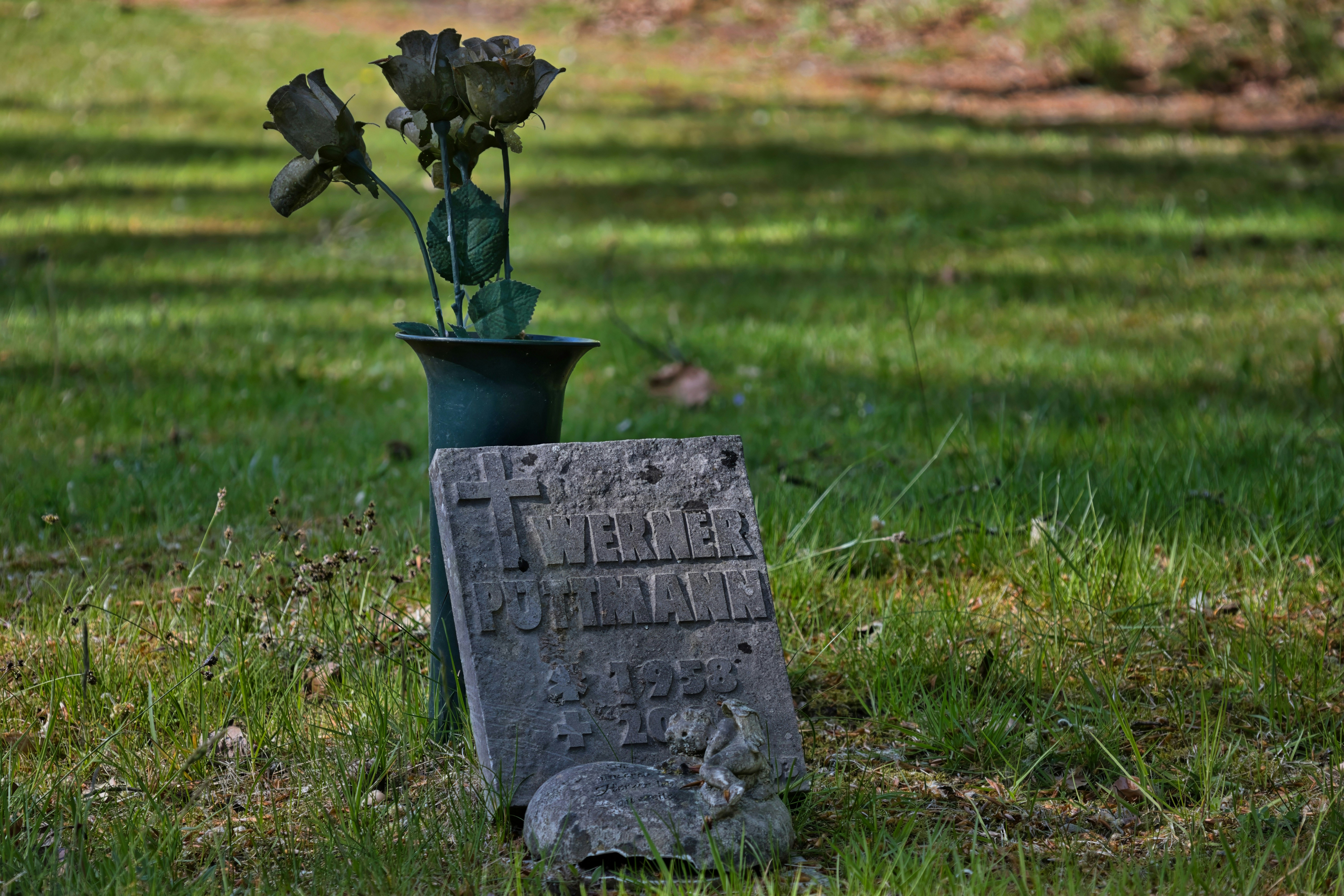 Memorial de mascotas con una figura de conejo de piedra y flores metálicas.