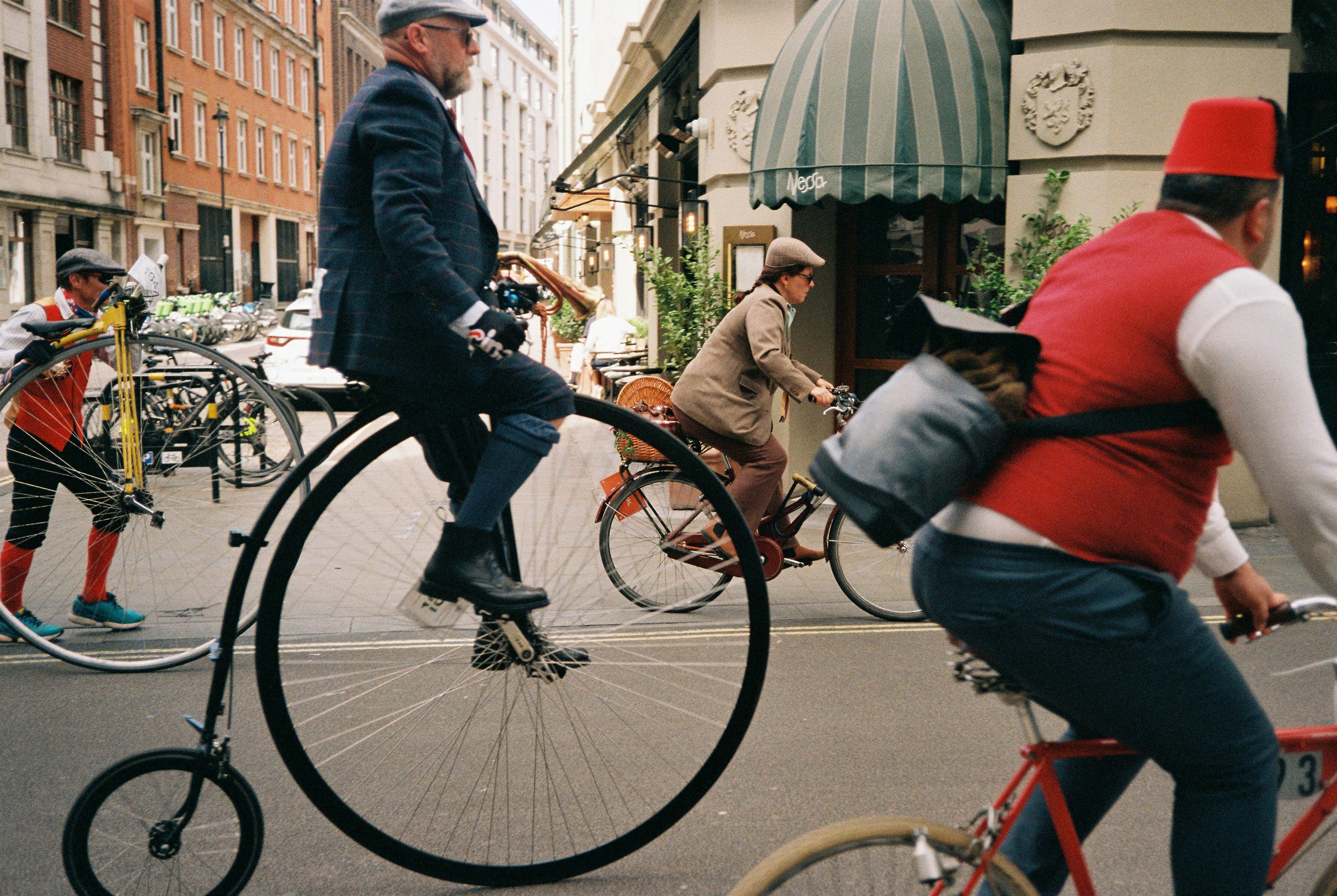 Men in vintage clothing riding bicycles on a street.