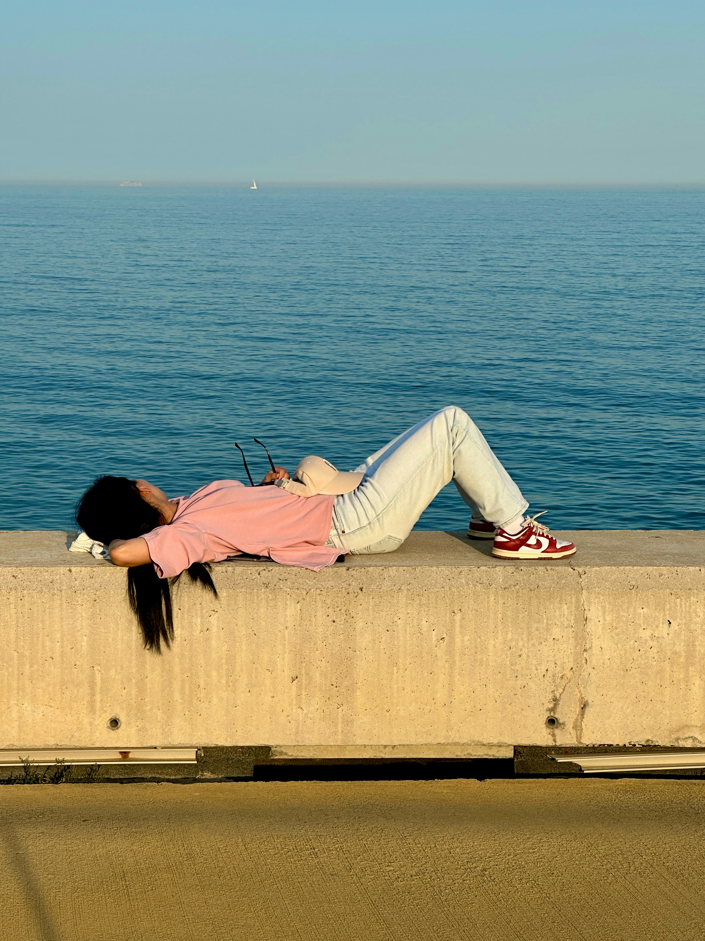 Woman relaxing on a concrete wall overlooking the sea.