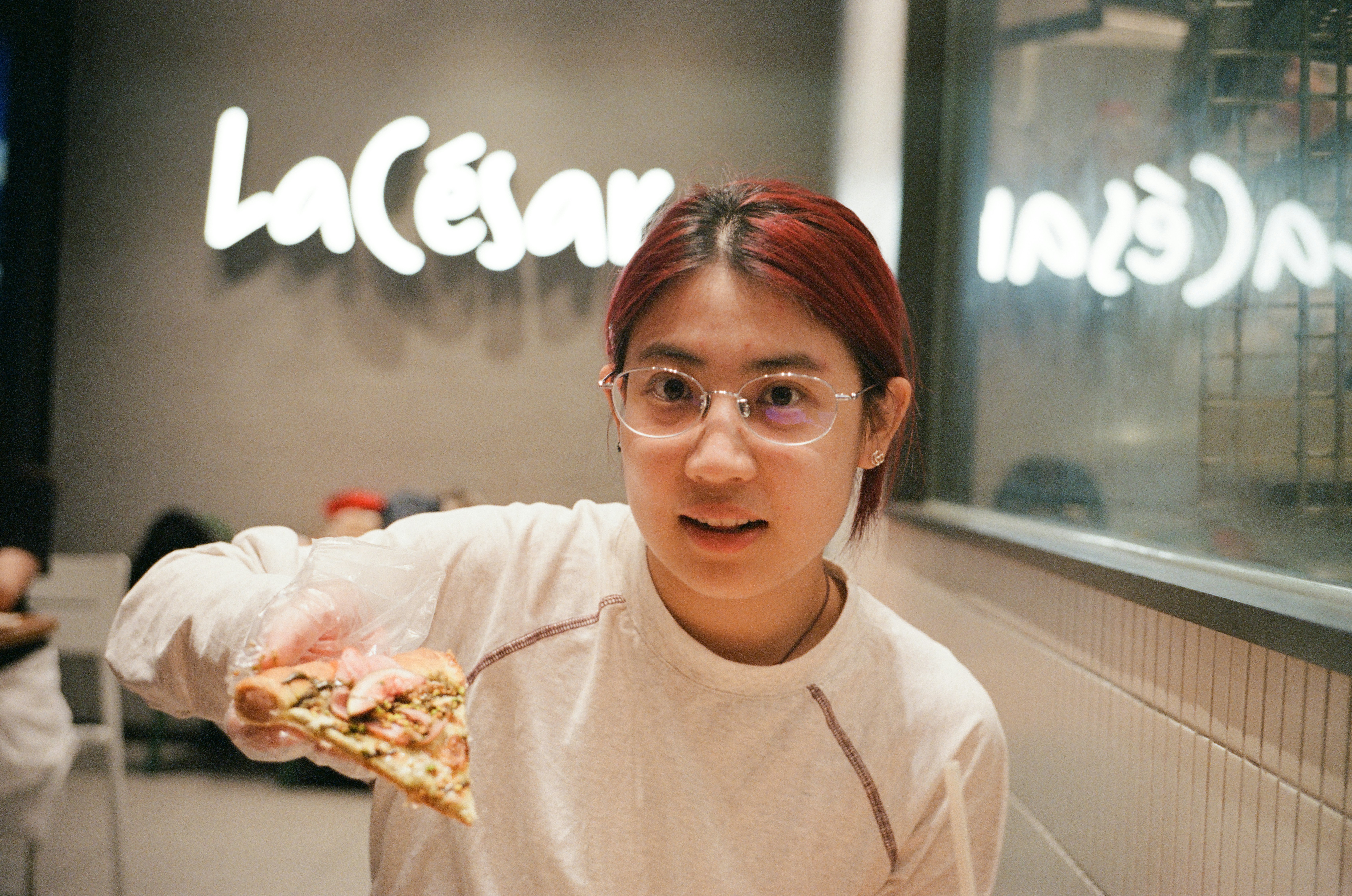 Young woman in glasses holding a pizza slice.
