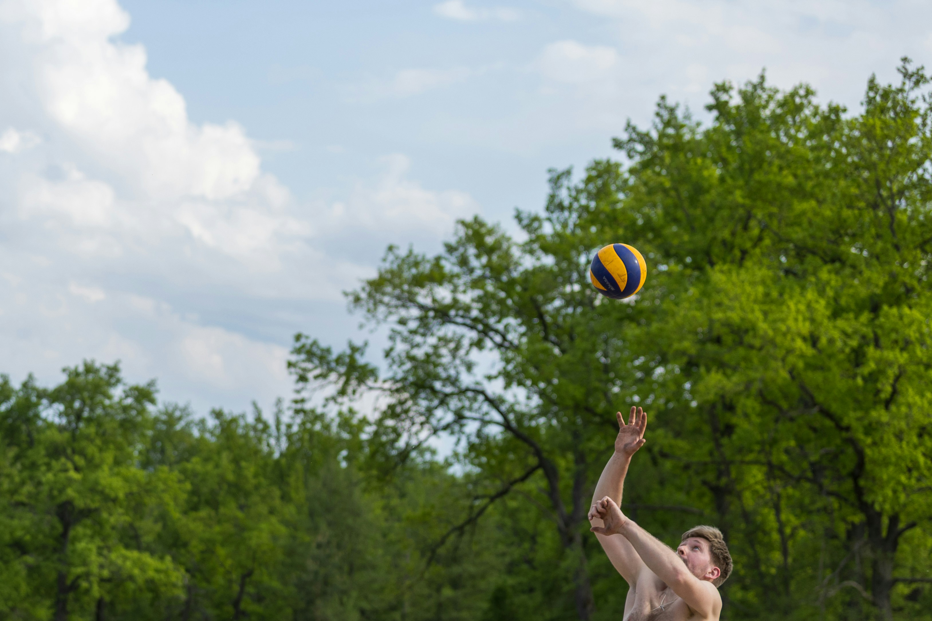 Mann, der draußen Volleyball spielt, mit Bäumen und Himmel.