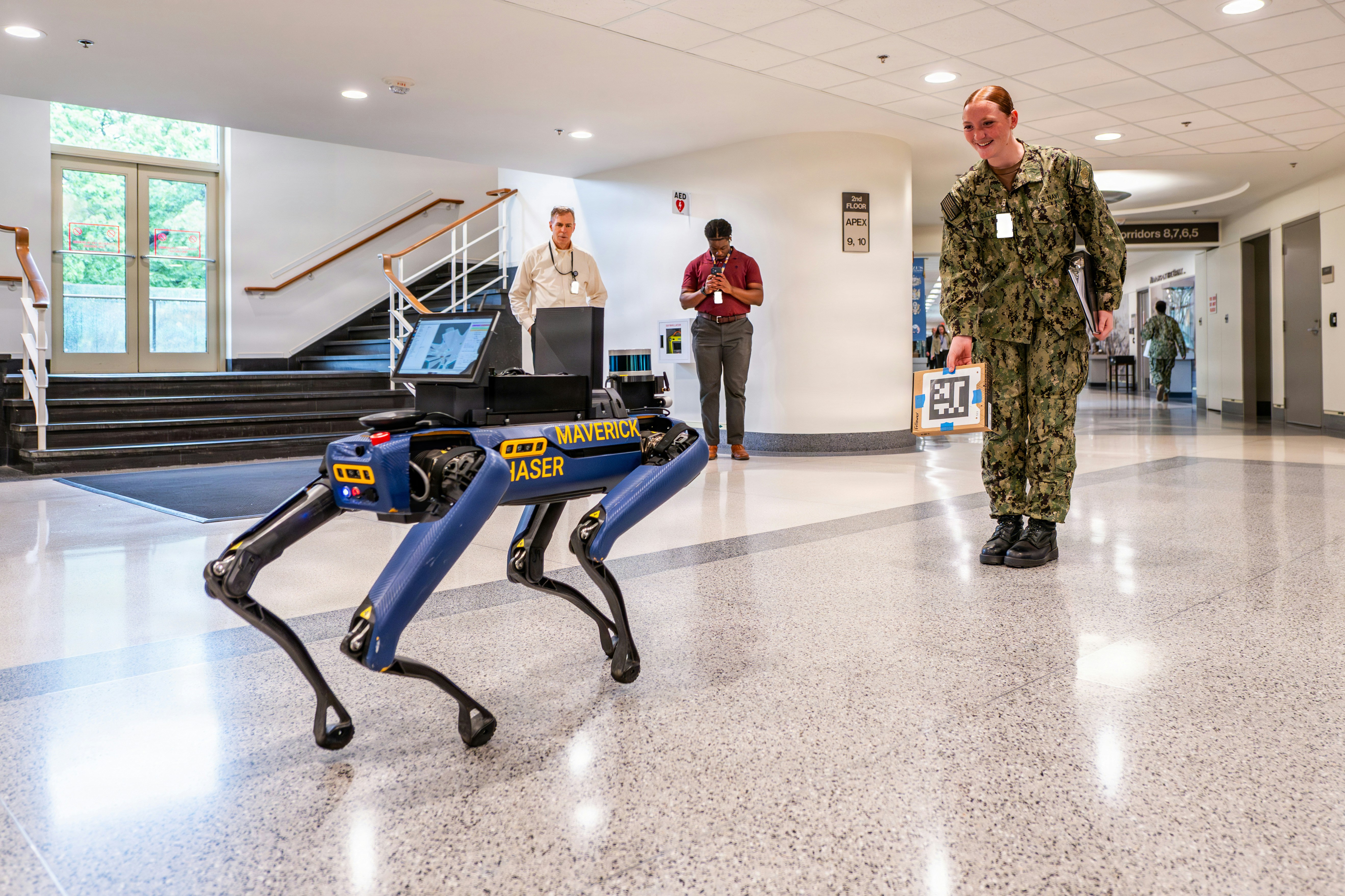 U.S. Navy Hospital Corpsman Seaman Madisen Marie Culler interacts with “Maverick,” a Collaborative Helper Autonomous Shipboard Exploration Robot, or CHASER, during the Department of War’s annual Lab Day at the Pentagon in Arlington, Virginia, May 6, 2026. The robot has sensors and software developed by the Naval Information Warfare Center Pacific that enable 3D mapping of the interior of a GPS-denied environment, such as a room, ship, or cave, and transmits that rendering to increase situational awareness. (U.S. Army photo by Bernardo Fuller) (This photo was altered for security purposes by blurring out identification badges.)