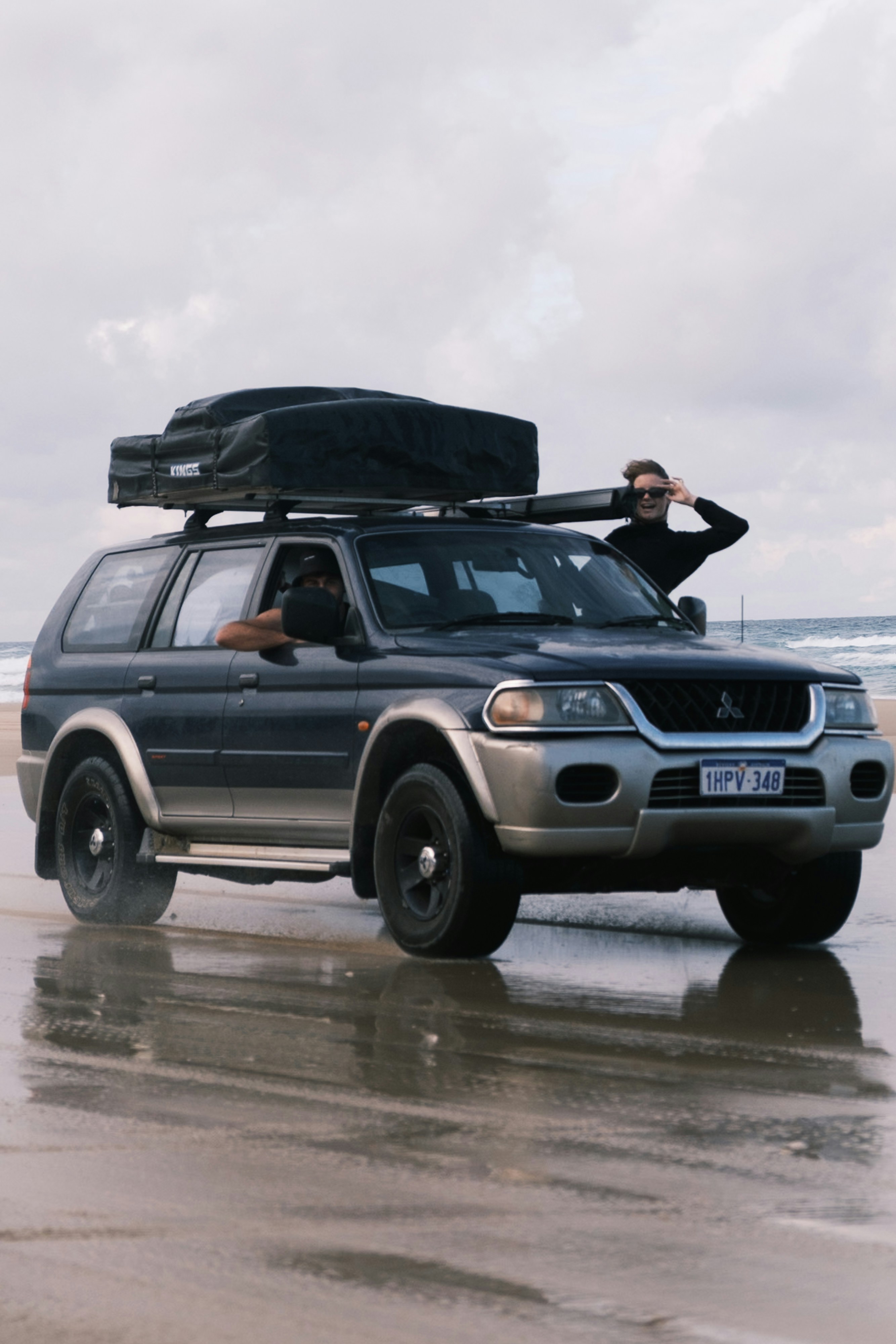 Dark suv with rooftop tent on a wet beach.