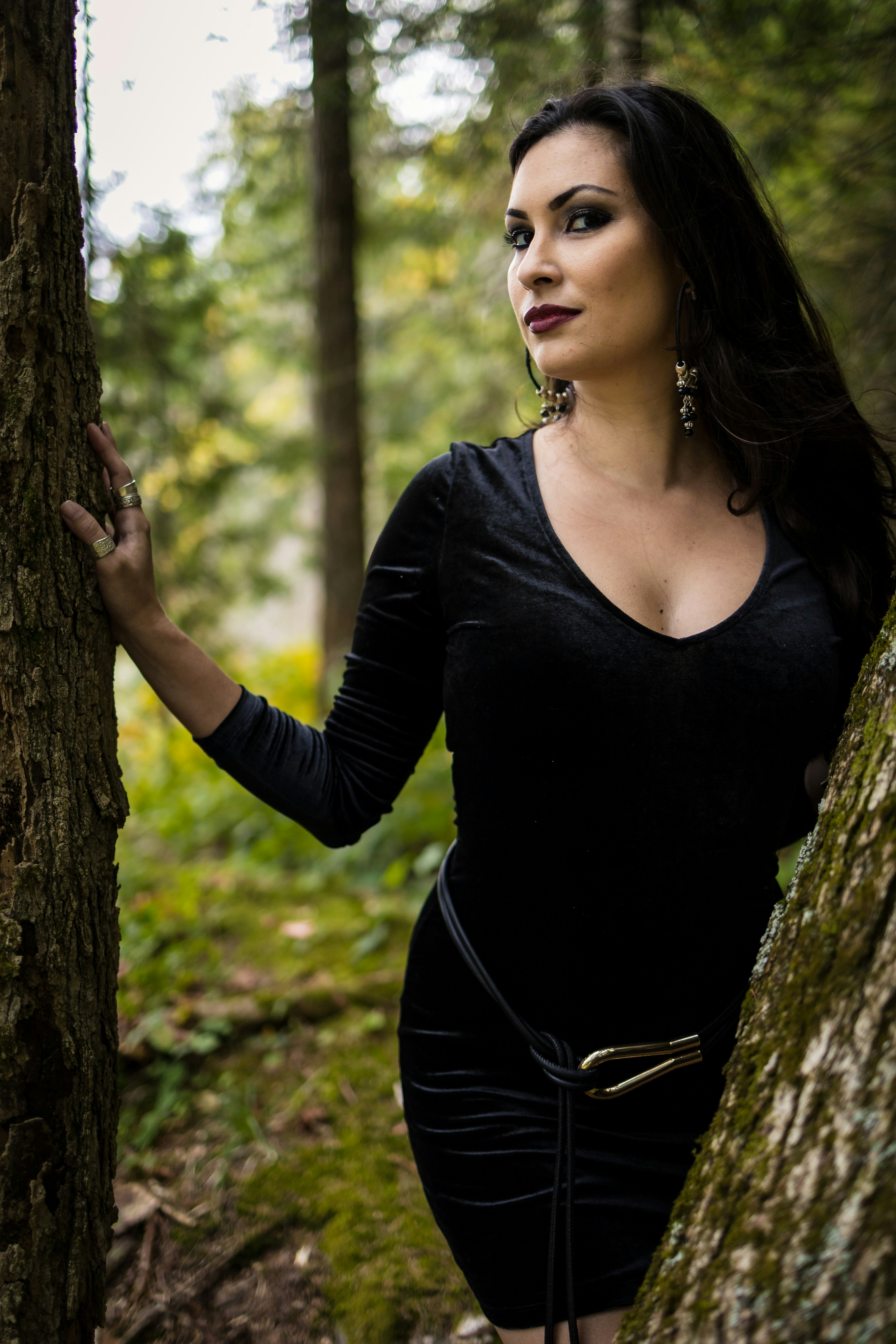 Woman in black dress posing in a forest.