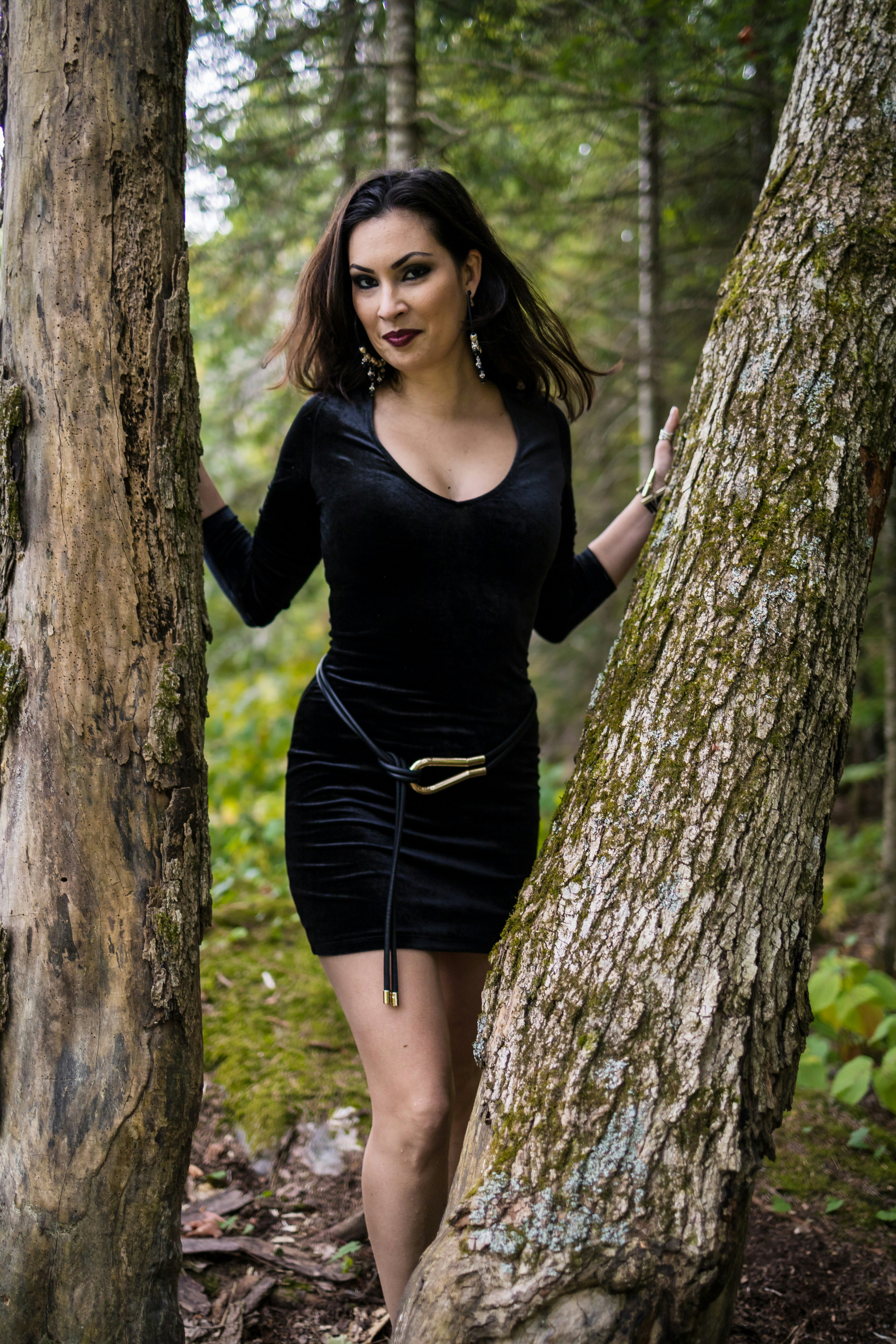 Elegant woman in black dress standing between two trees.