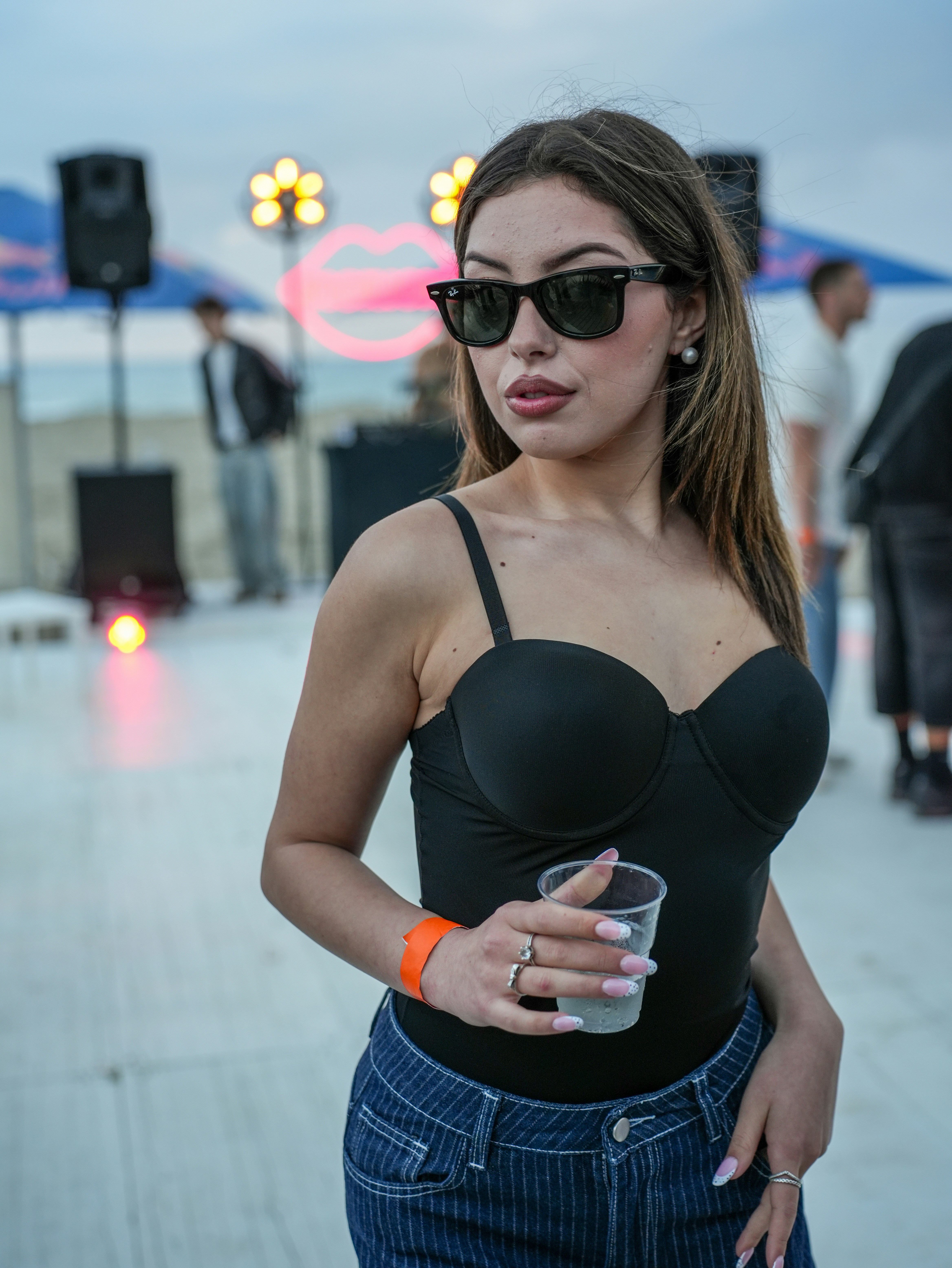 A young woman wearing sunglasses holds a drink outdoors.