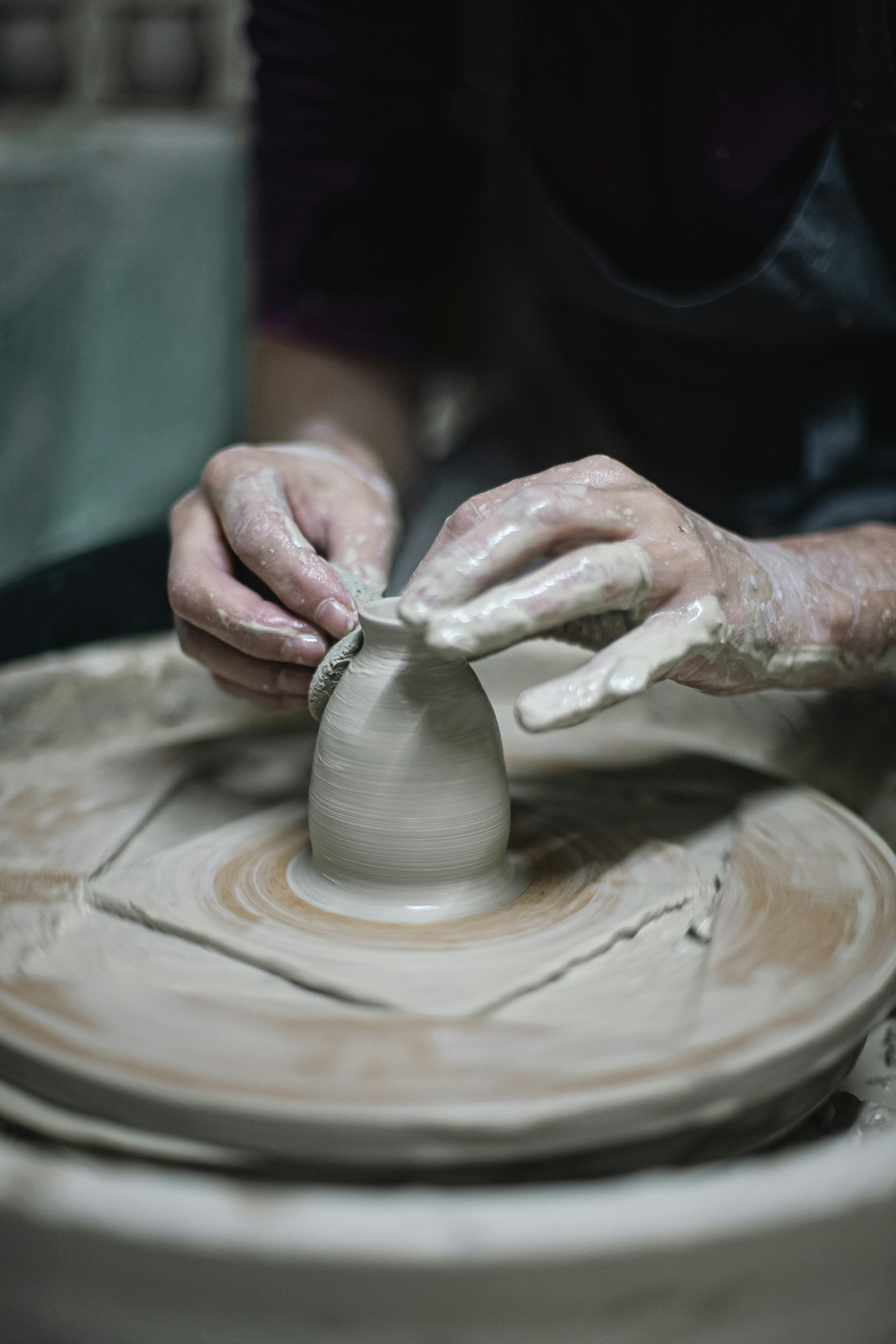 Hands shaping clay on a pottery wheel