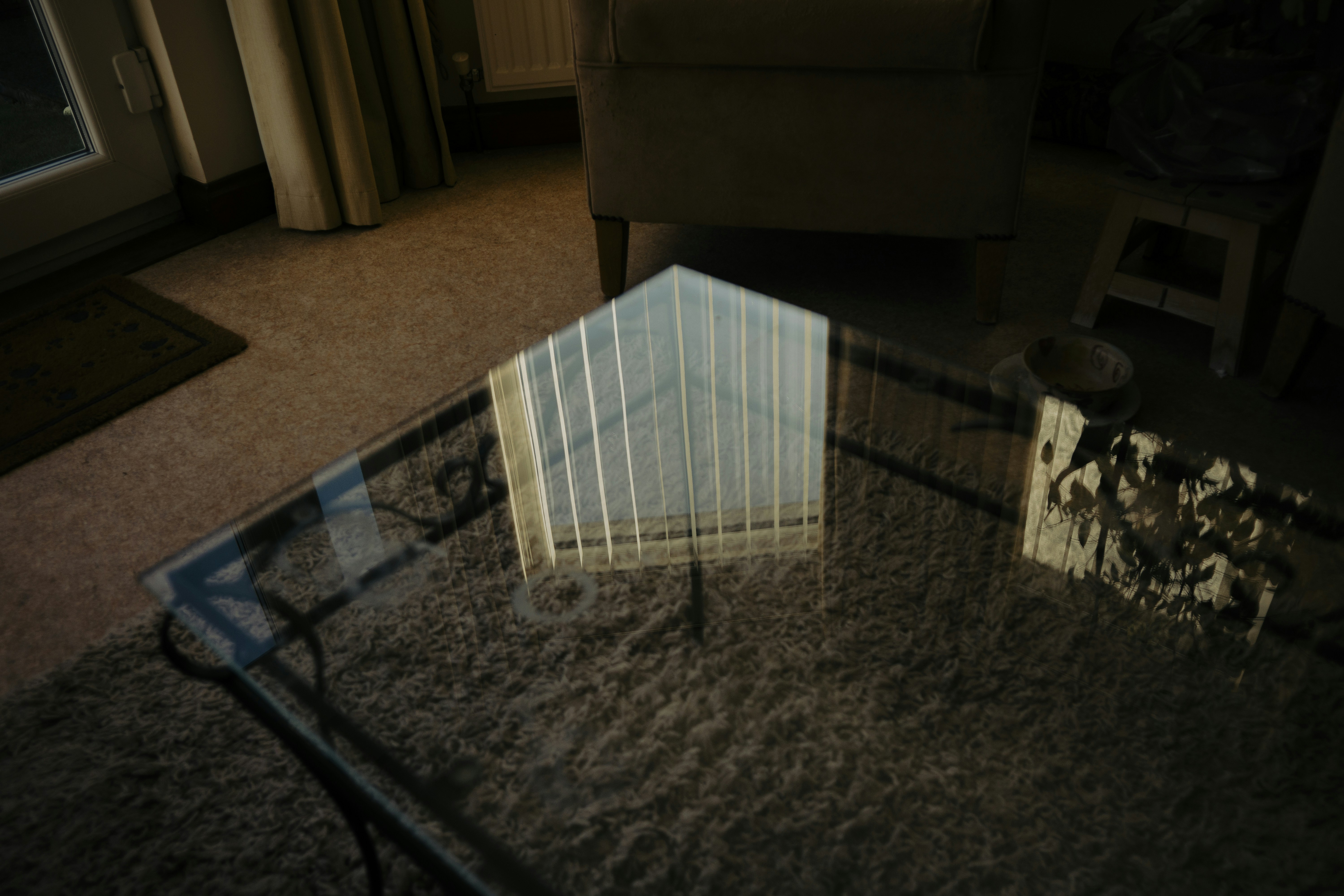 Glass coffee table with reflection of vertical blinds.