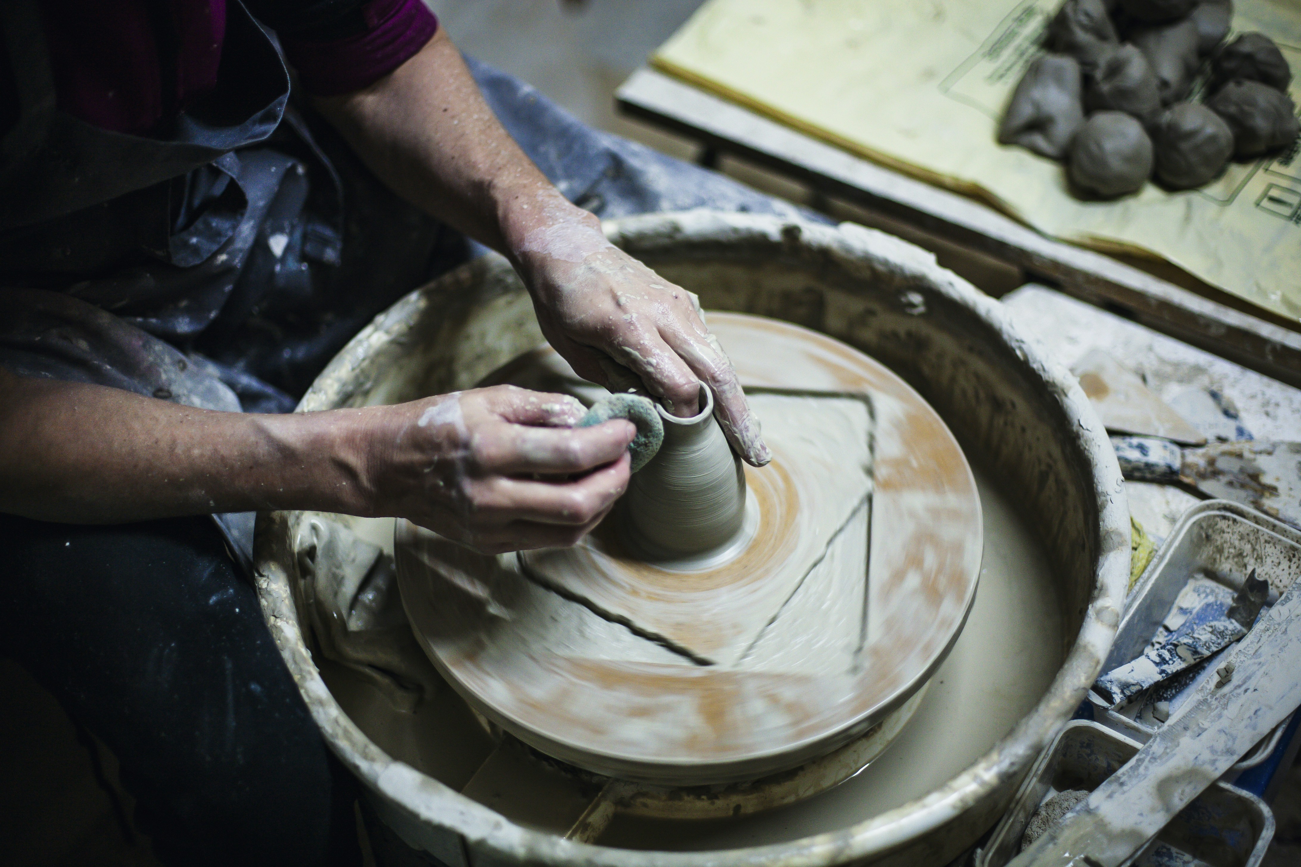 A person's hands shaping clay on a pottery wheel.