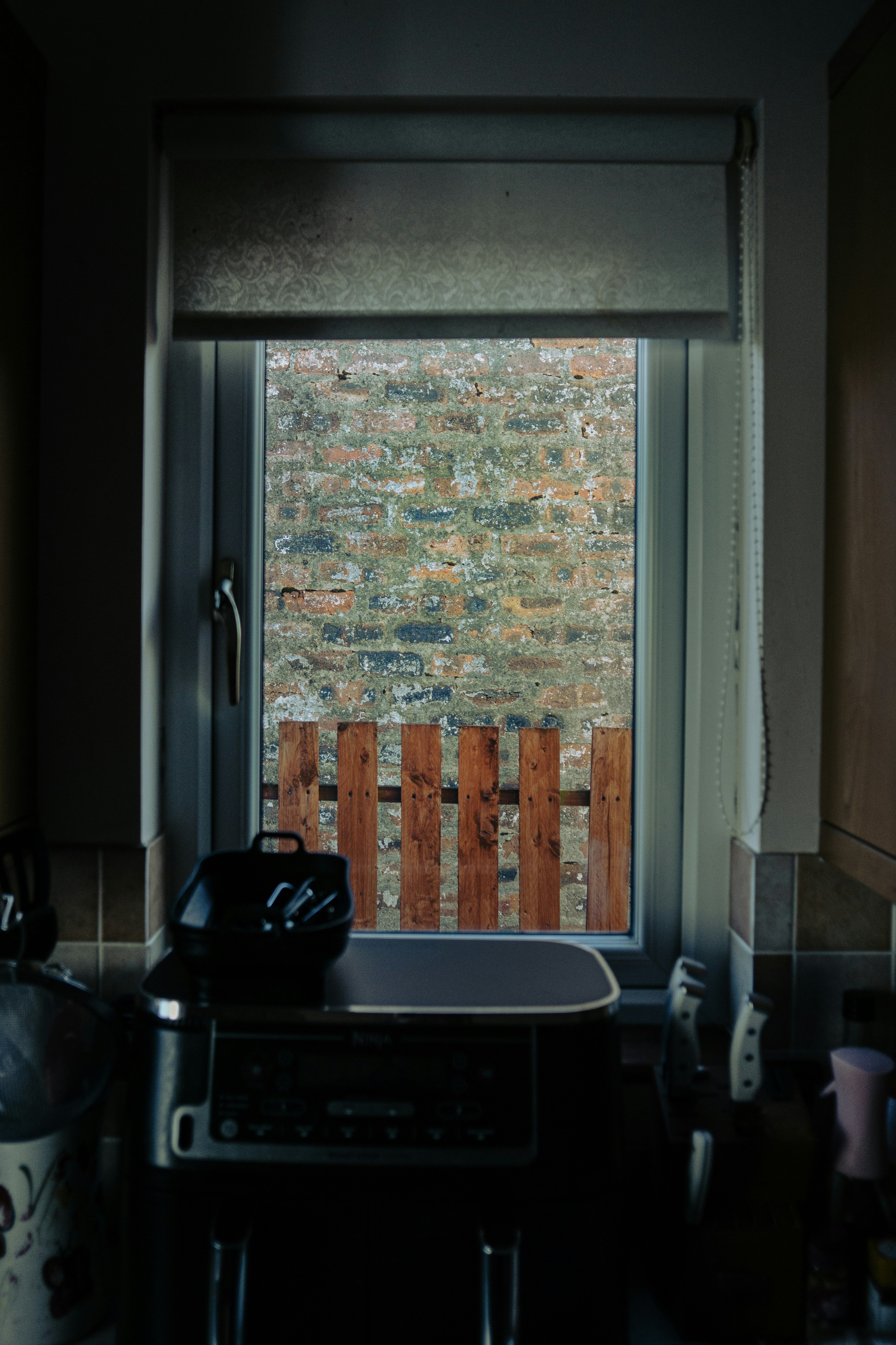 Window view of a brick wall and small wooden barrier.