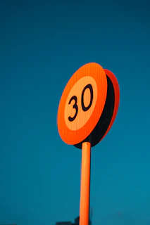 Orange speed limit sign showing 30 against blue sky.
