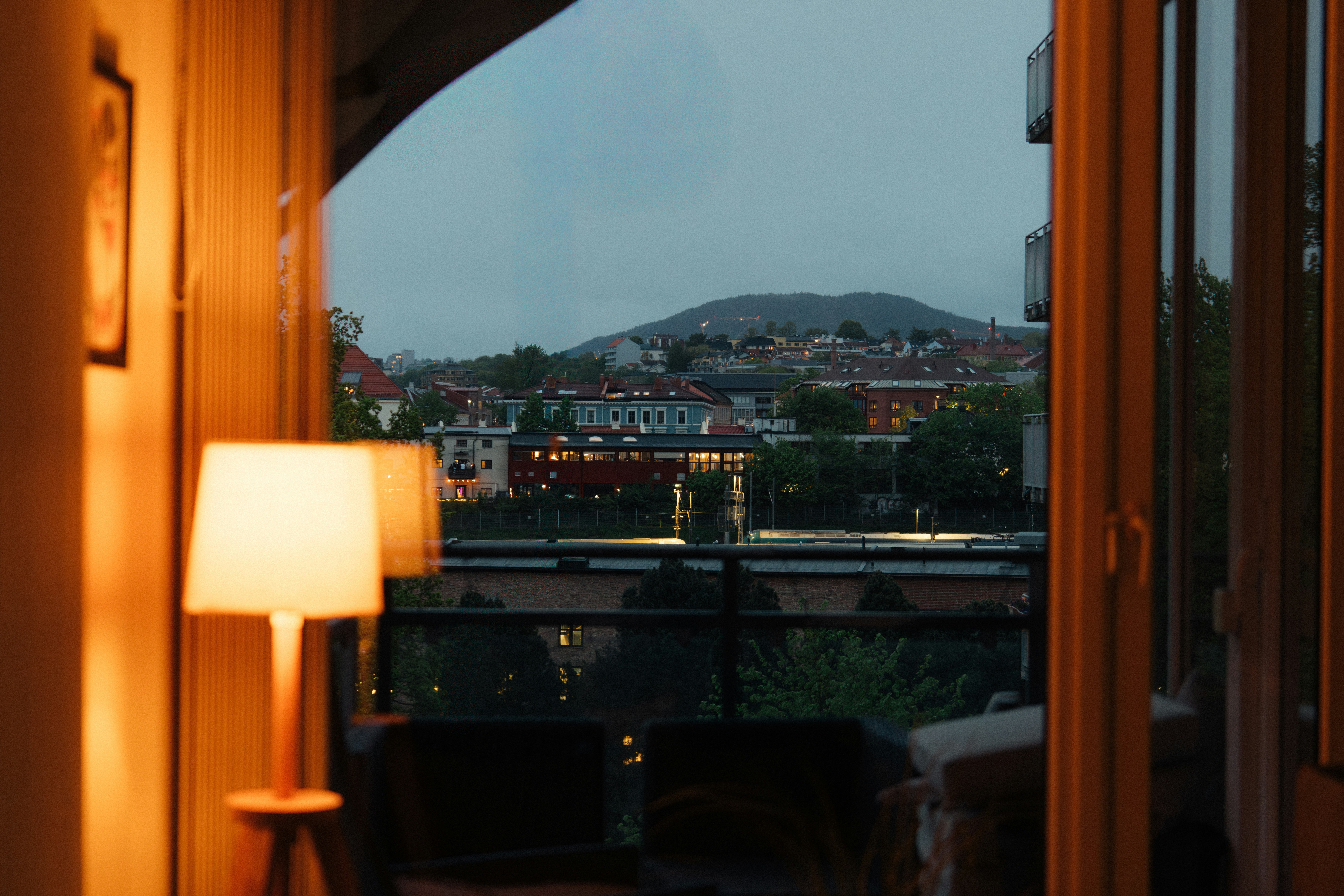 A warm lamp illuminates an evening city and distant mountain.