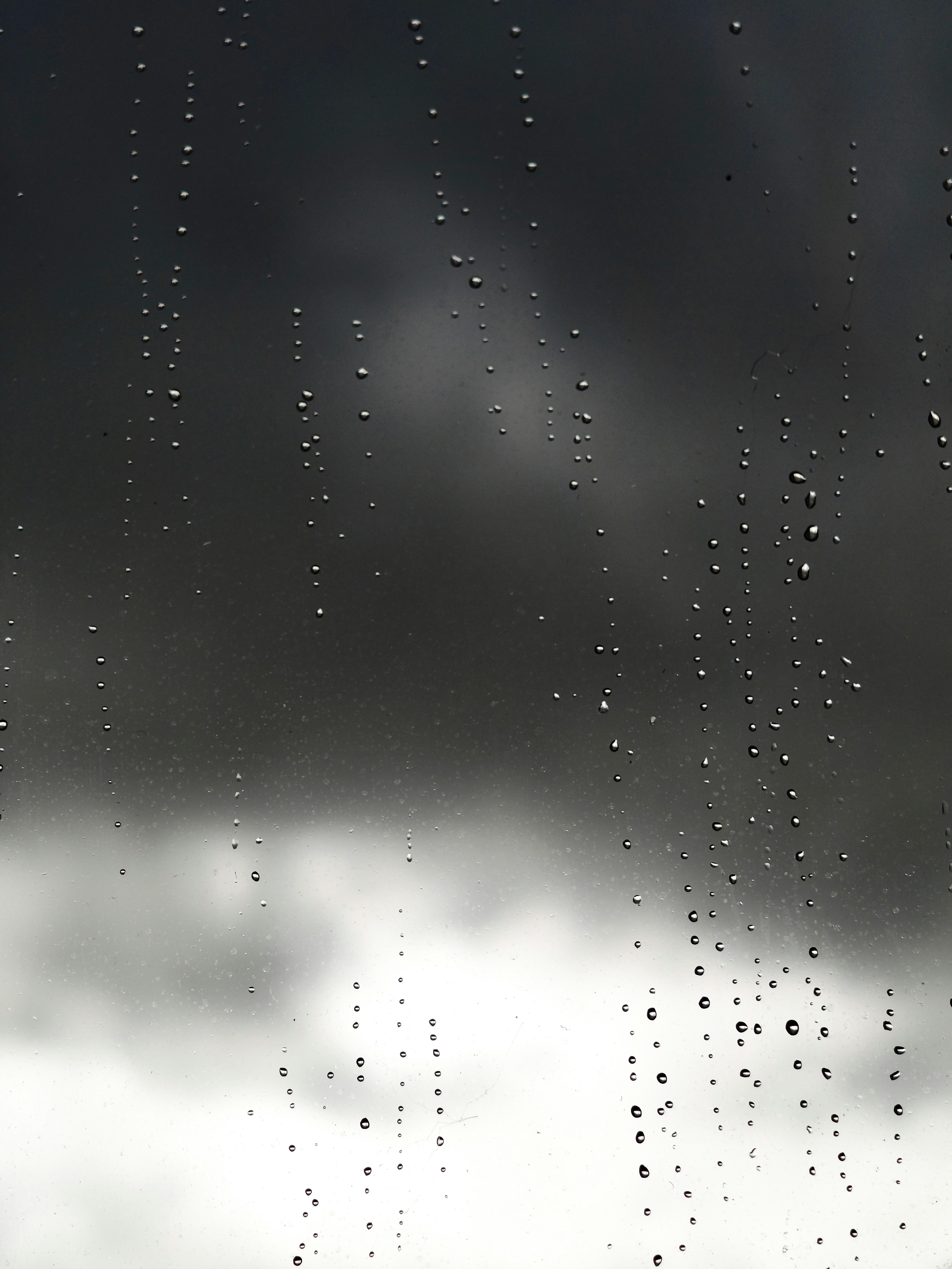 Raindrops on a window against a dark, cloudy sky.