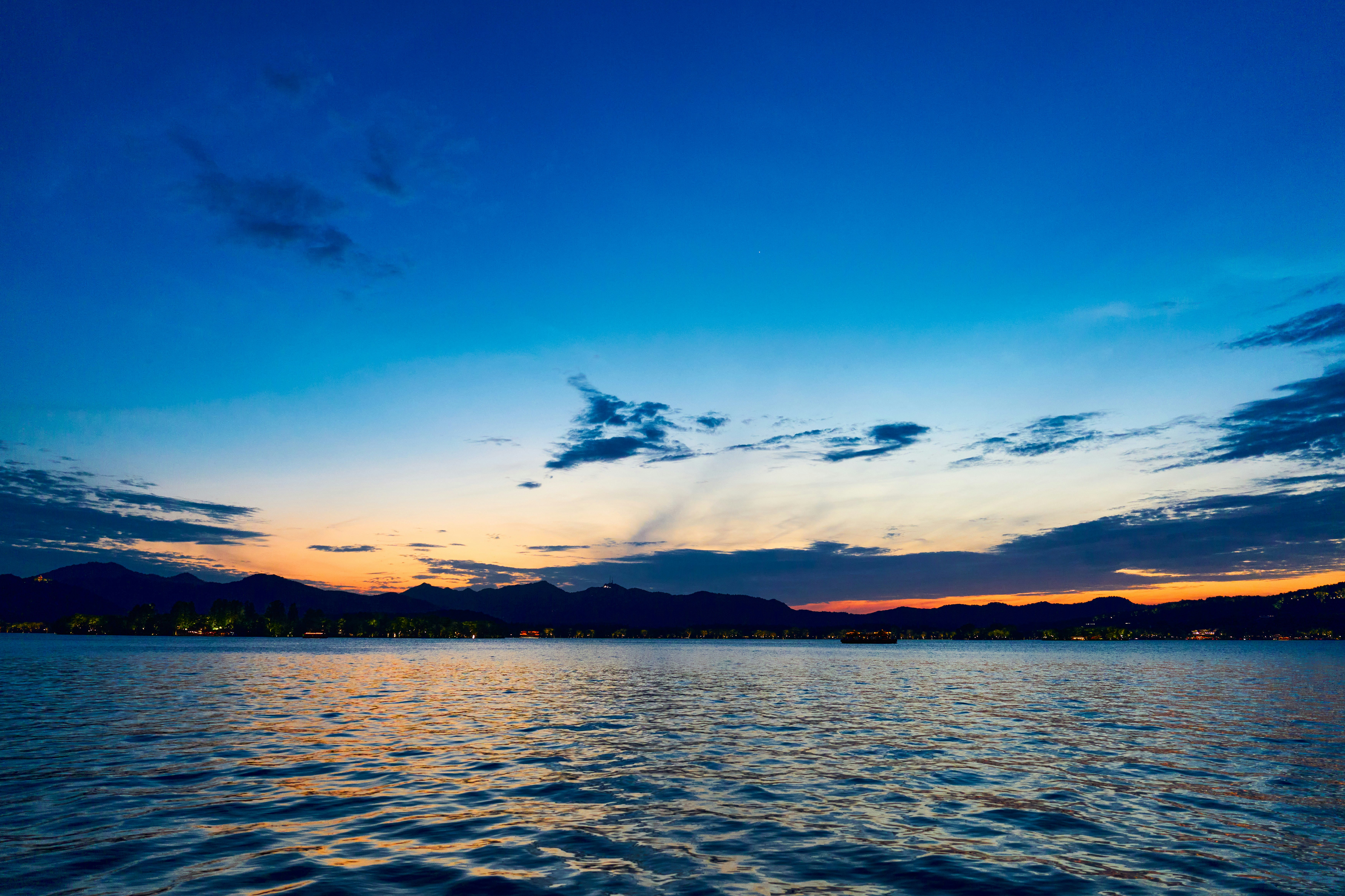 Céu crepuscular sobre um lago calmo com luzes distantes da cidade.