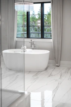 Modern bathroom with a white freestanding bathtub and large window.