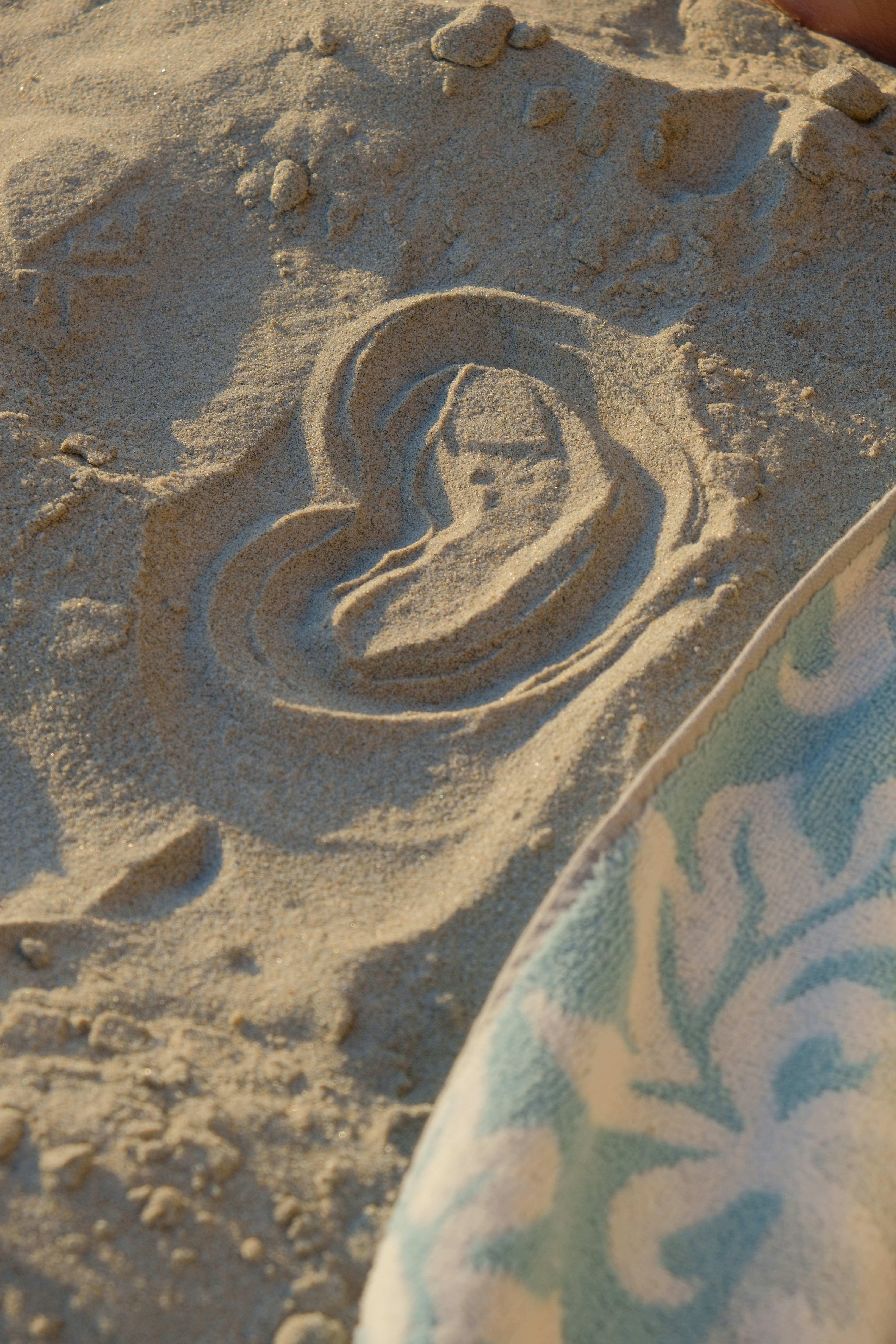 Ein Herz in Strandsand gezeichnet mit einem gemusterten Handtuch.