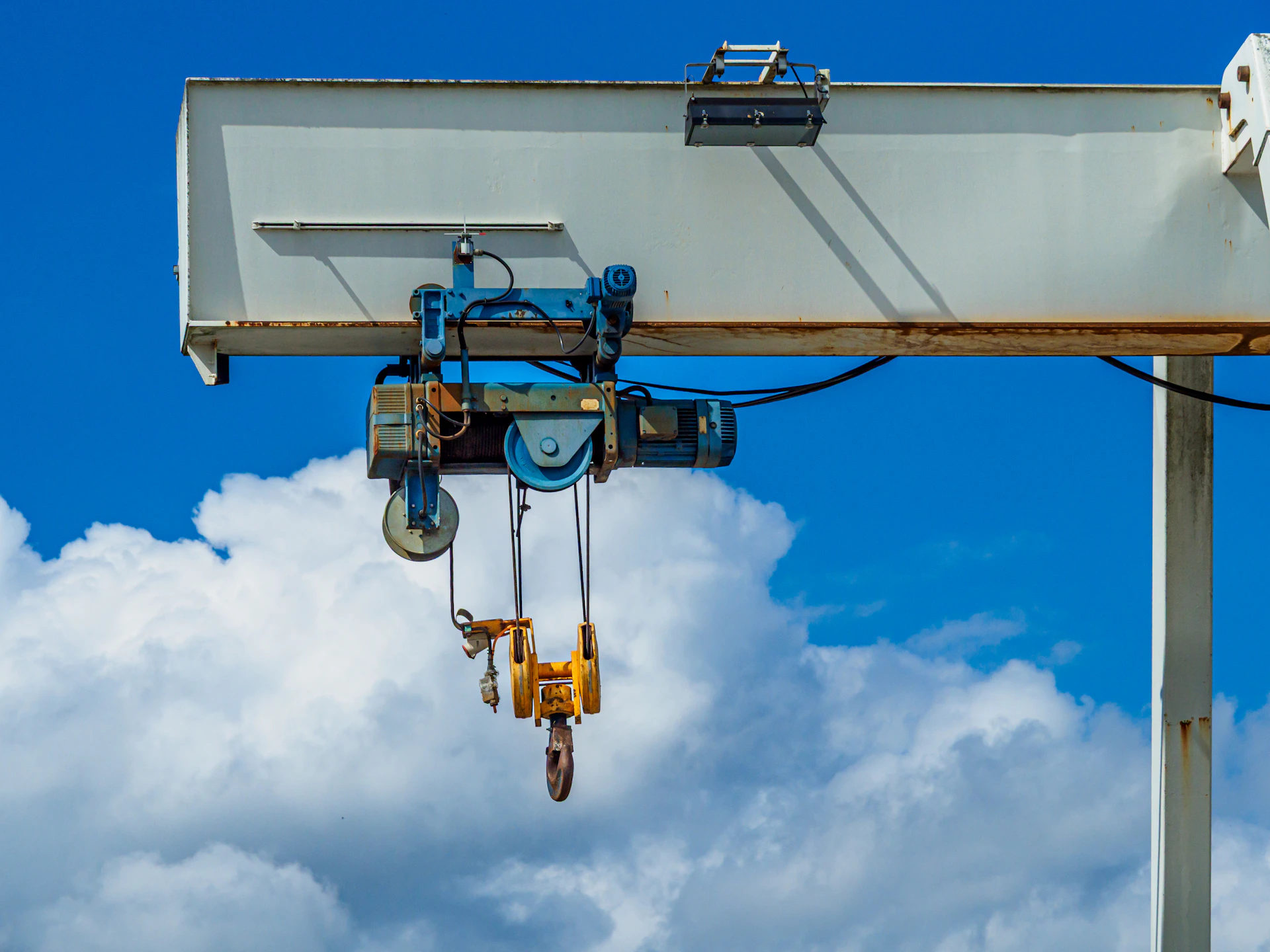 Industrial gantry crane with hooks against a blue sky.