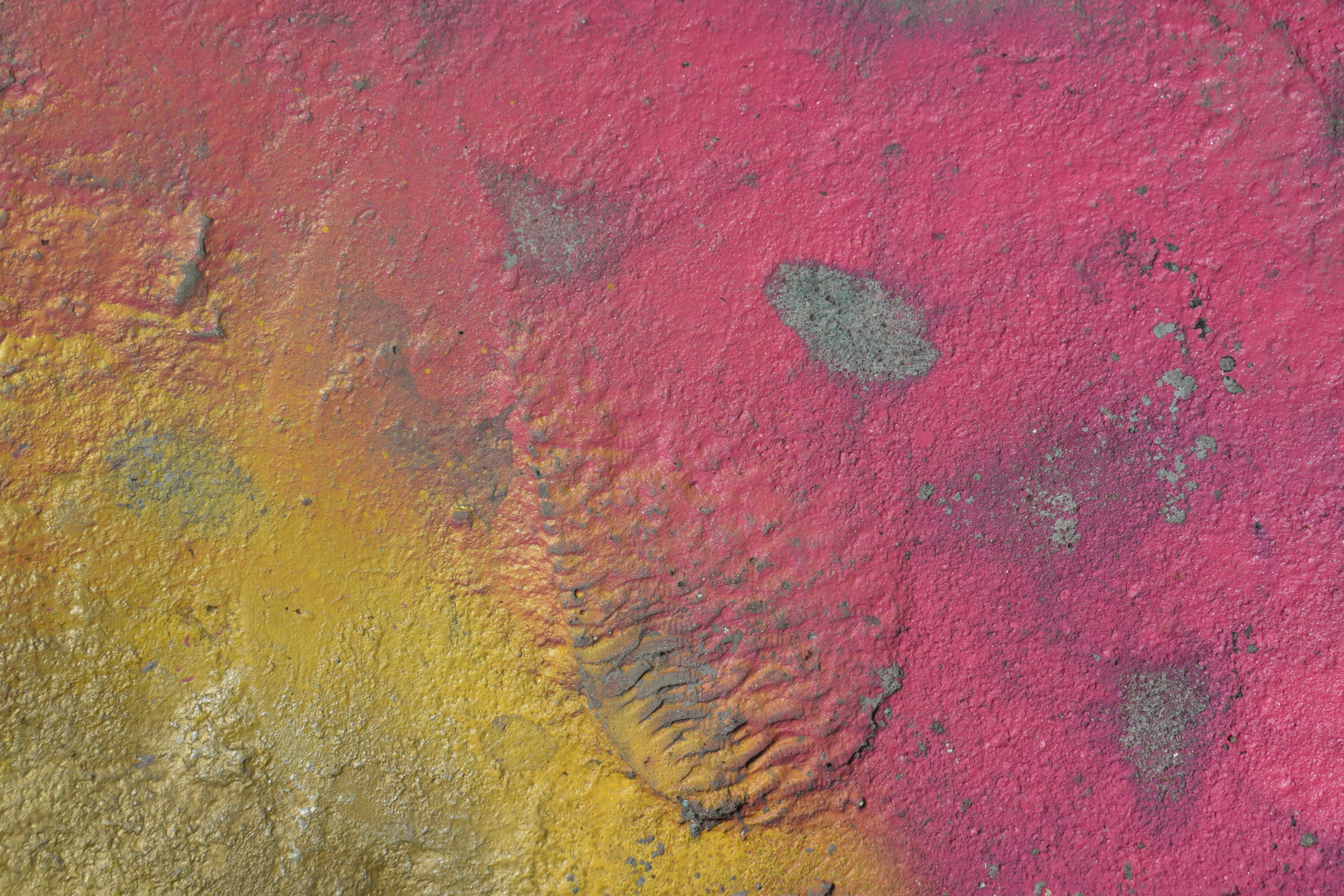 Textured surface with pink and yellow paint and grey patches.