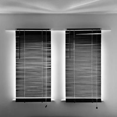 Two windows with closed horizontal blinds, glowing edges.
