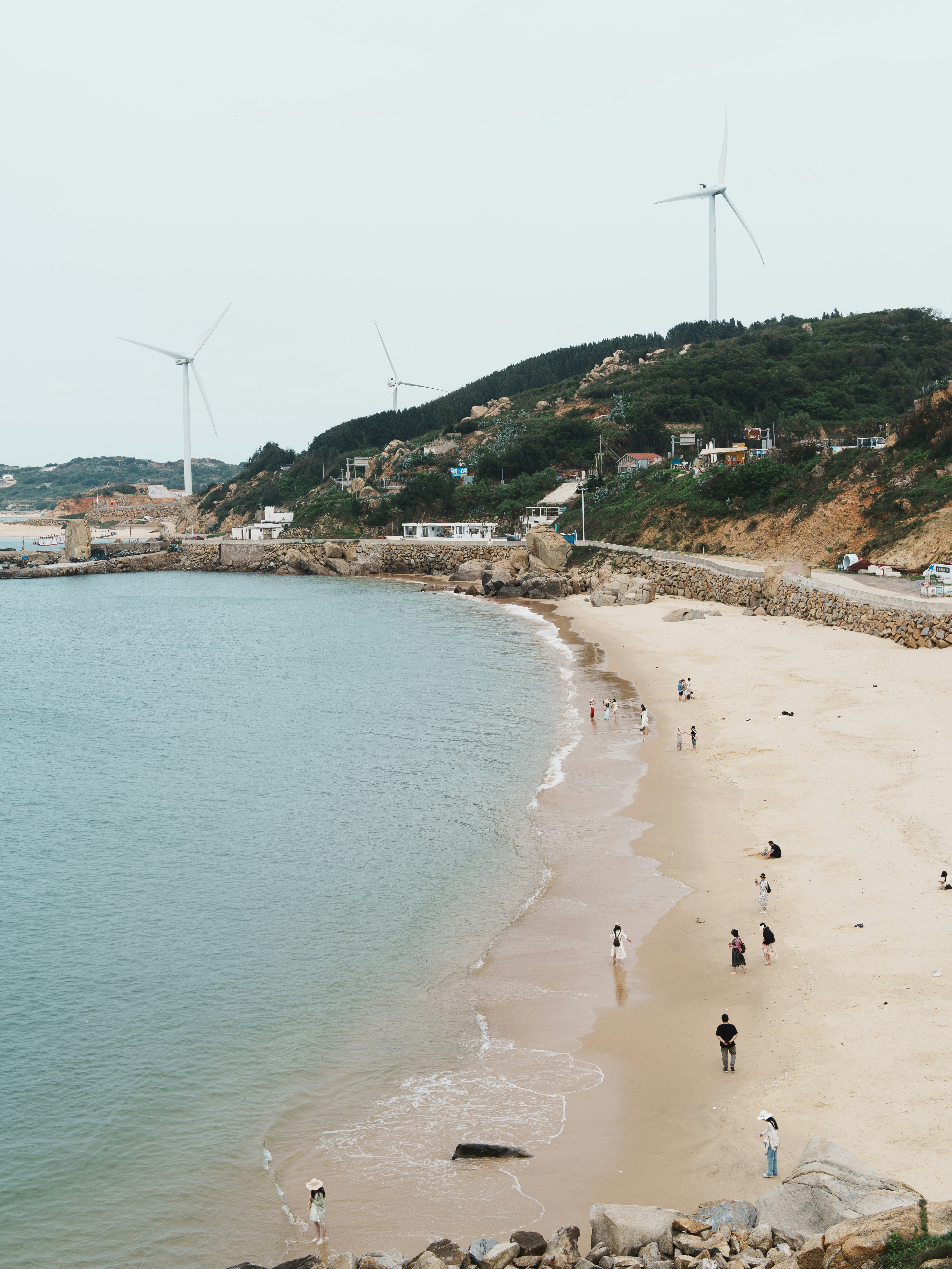 Gente disfrutando de una playa con aerogeneradores en las colinas.