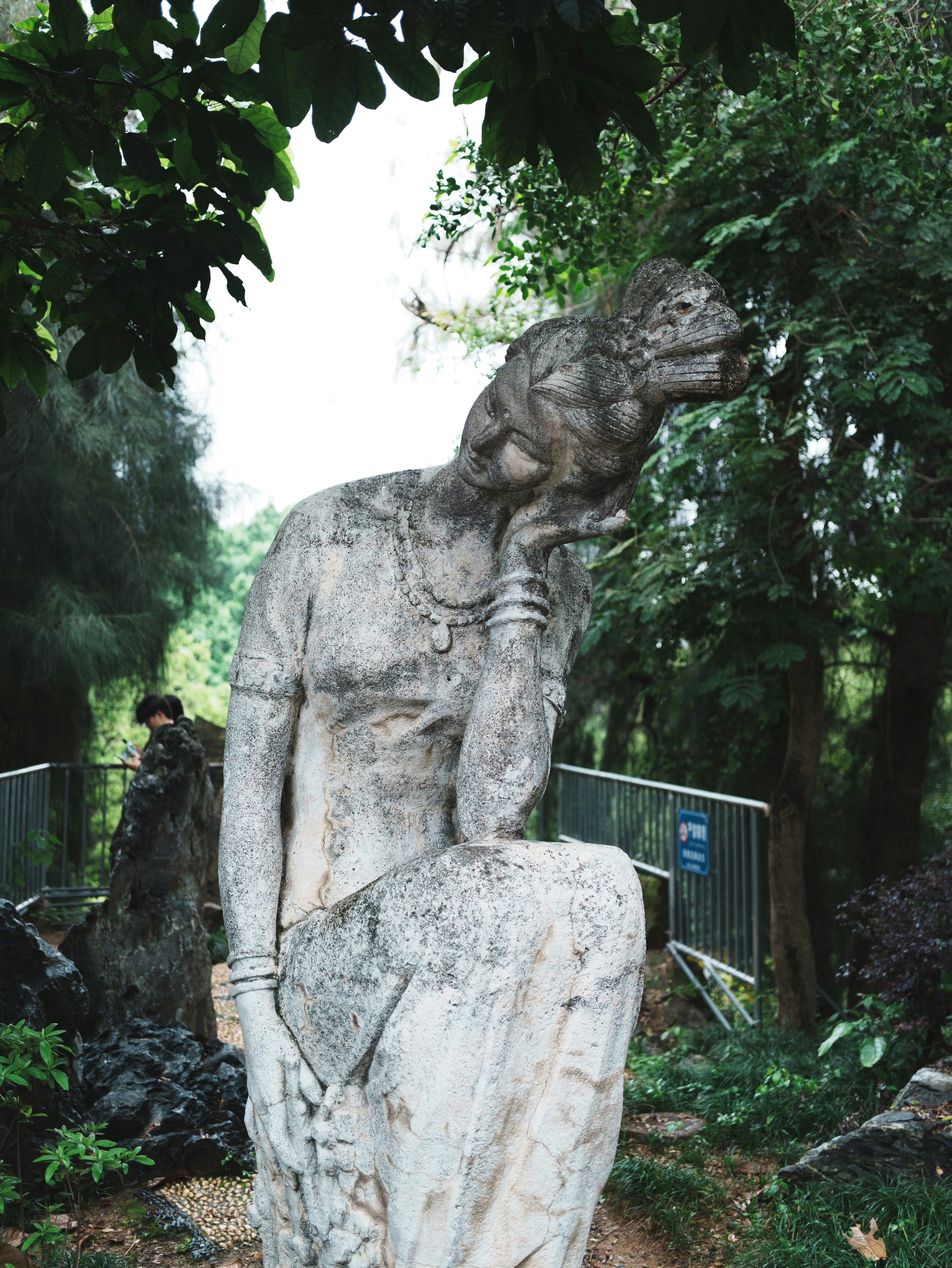 Statua di pietra di una donna in posa pensierosa all'aperto.