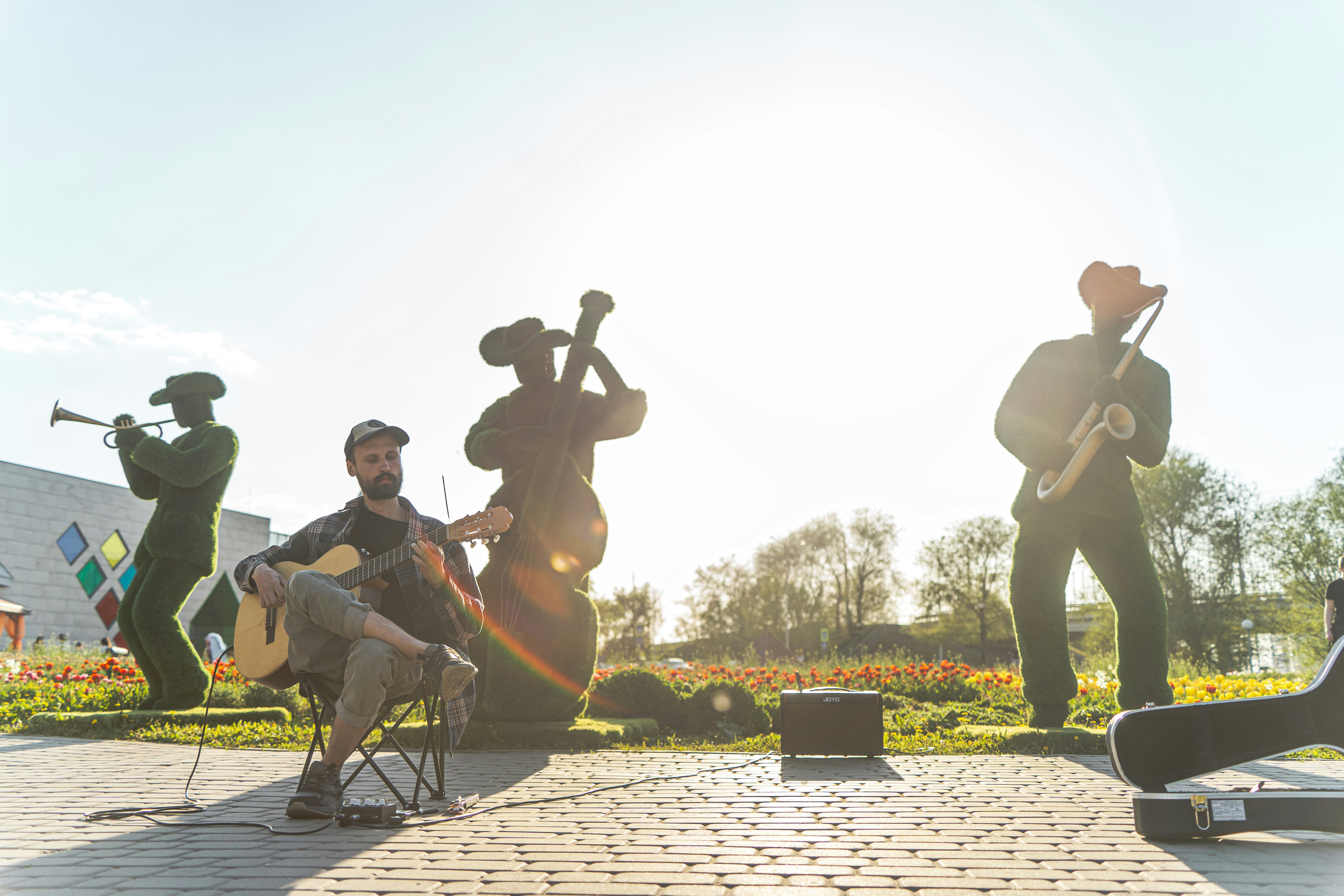 Musicians playing instruments outdoors with statues behind them